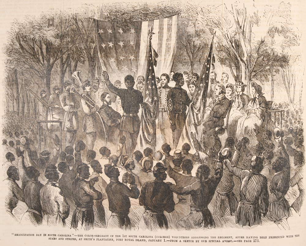 An archival black-and-white wood engraving titled "Emancipation Day in South Carolina." The illustration depicts a large, celebratory gathering at Smith’s Plantation on Port Royal Island on January 1, 1863. At the center of the scene, a Black soldier—identified in the caption as the Color-Sergeant of the 1st South Carolina (Colored) Volunteers—stands on a raised platform, gesturing with one arm raised as he addresses a massive crowd. He is flanked by other soldiers holding upright American flags.  Behind the speaker, a brass band with horns and drums is visible, along with several seated and standing white and Black observers under the shade of large trees. In the background, a massive American flag is draped horizontally between the trees.  The foreground is filled with the backs of a dense crowd of Black men, women, and children, many with their hands raised in celebration or holding hats in the air. The caption at the bottom provides historical context, noting the event followed the presentation of the "Stars and Stripes" to the regiment.