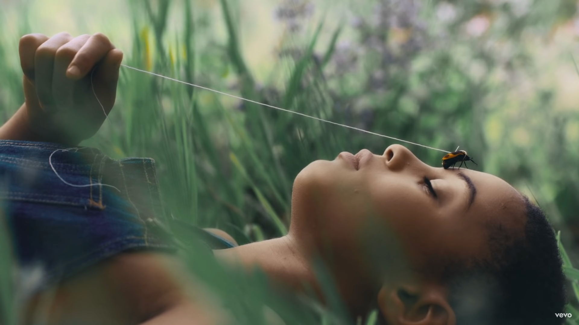 A cinematic, close-up profile shot of a person lying peacefully on their back in a lush, green meadow.