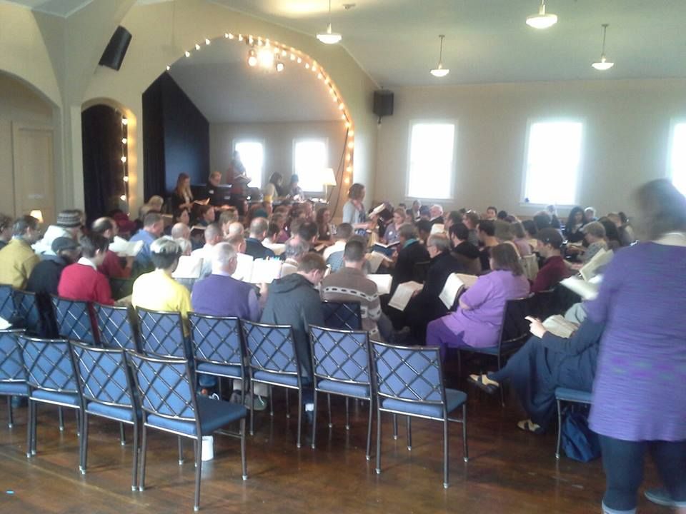Group of people seated in a square formation singing Sacred Harp shape-note music.