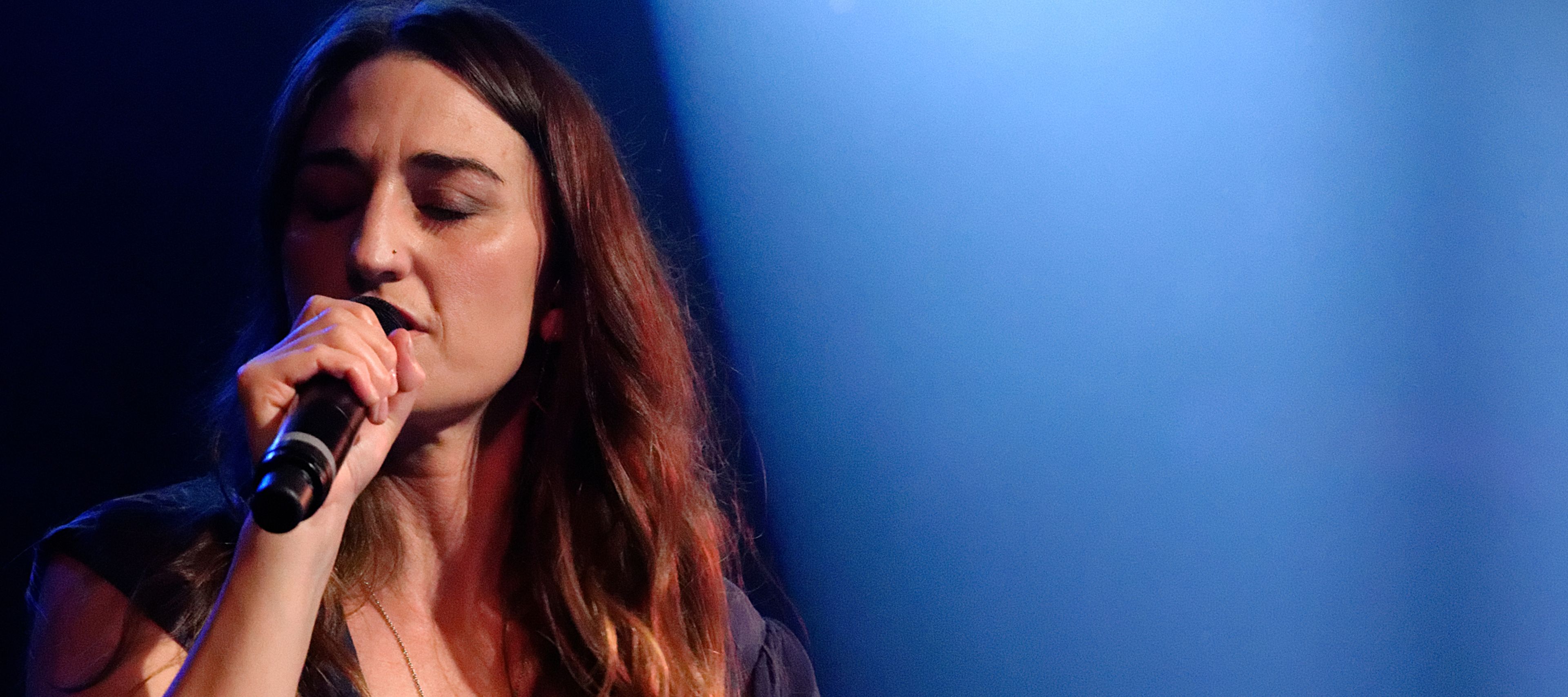 Sara Bareilles sings into a microphone with eyes closed