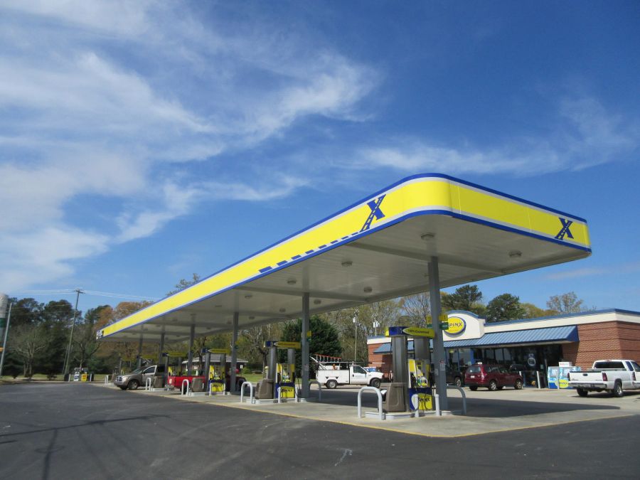 Canopy with a curved yellow and blue fascia over dispensers in front of a store