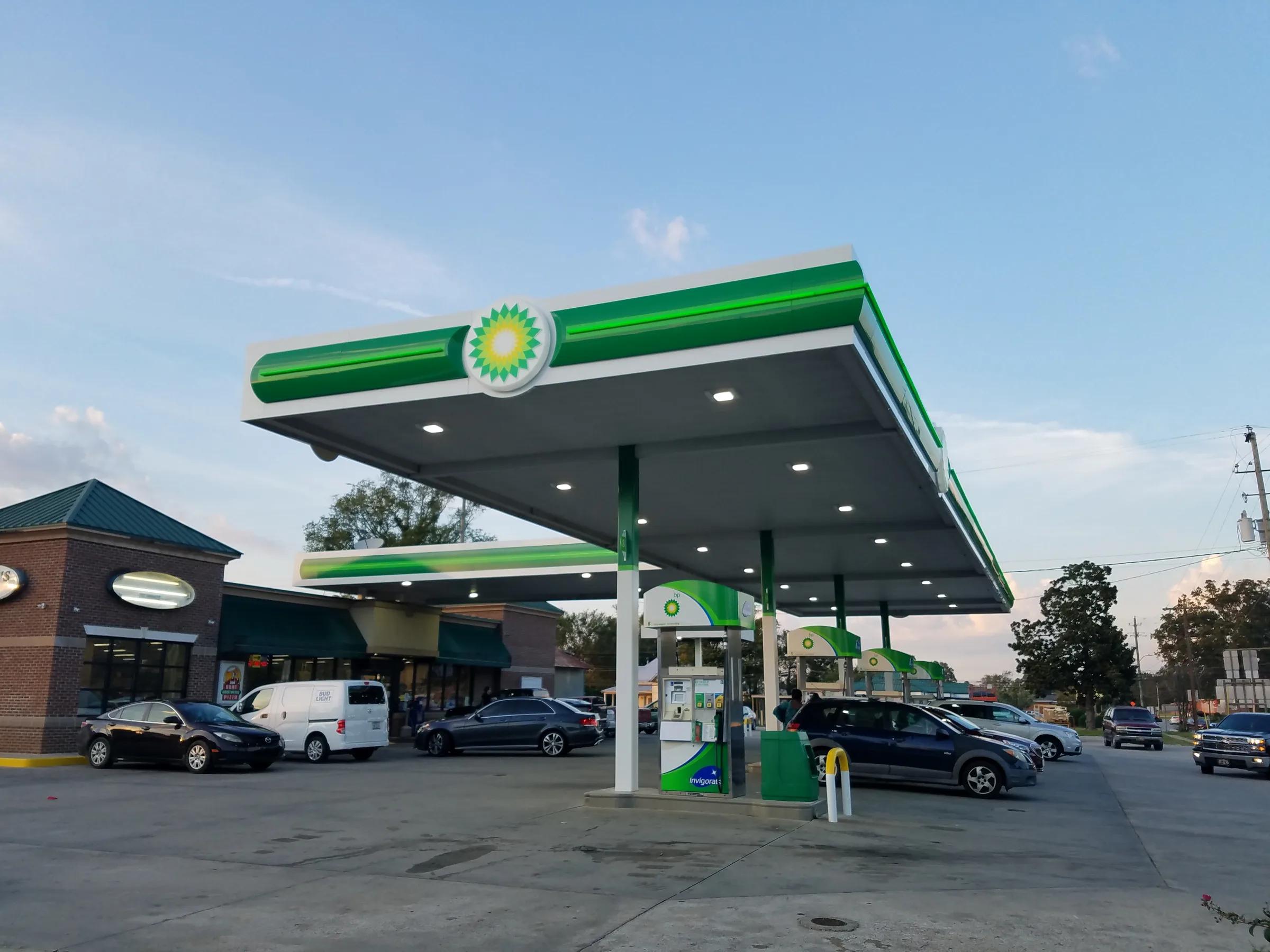 BP canopy with a green fascia and a lit BP sign over dispensers, shops behind
