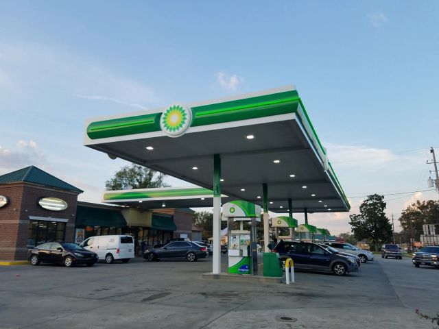 BP canopy with a green fascia and a lit BP sign over dispensers, shops behind