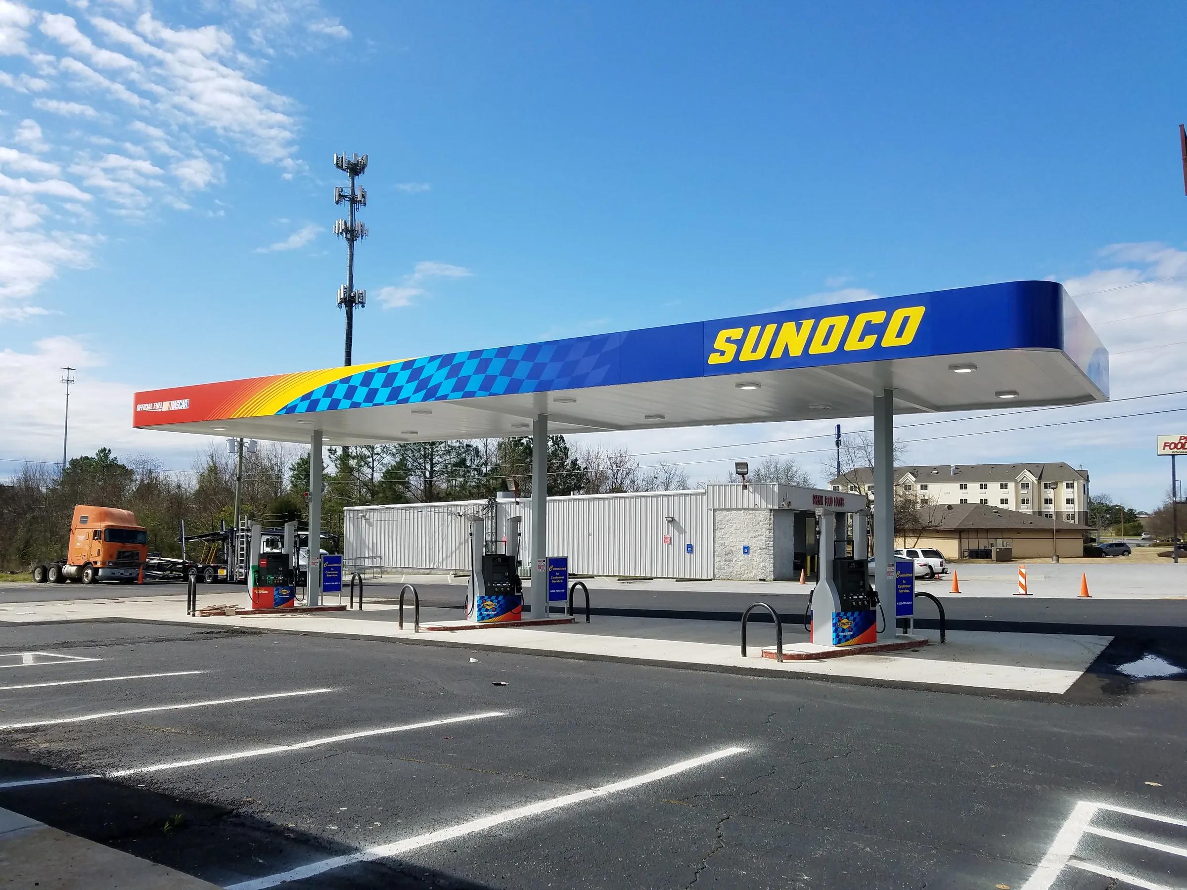 Sunoco canopy with a blue and checkered fascia over dispensers, a freshly striped lot in front