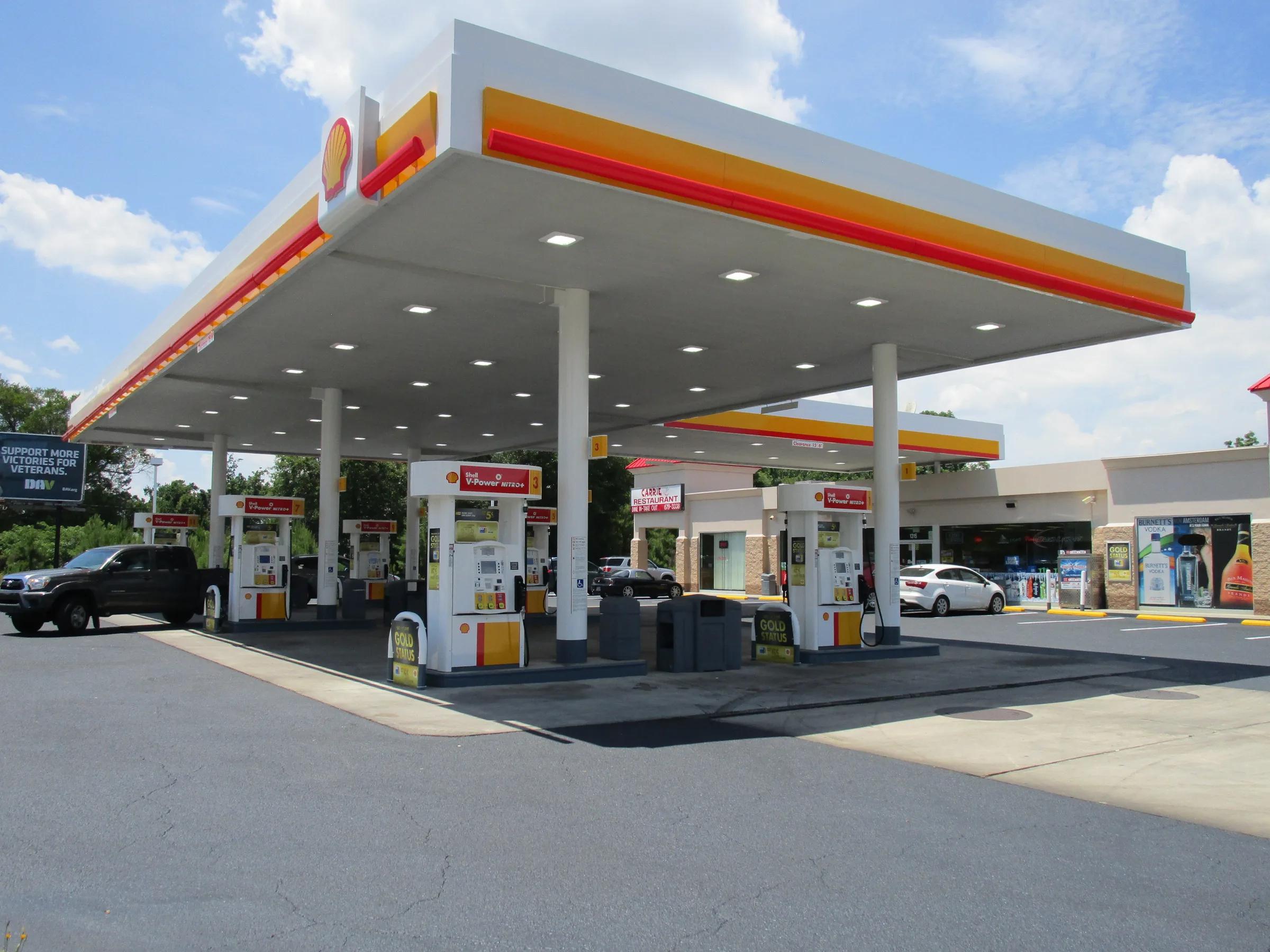 Shell canopy with a red and yellow fascia and recessed lights over dispensers in front of a store