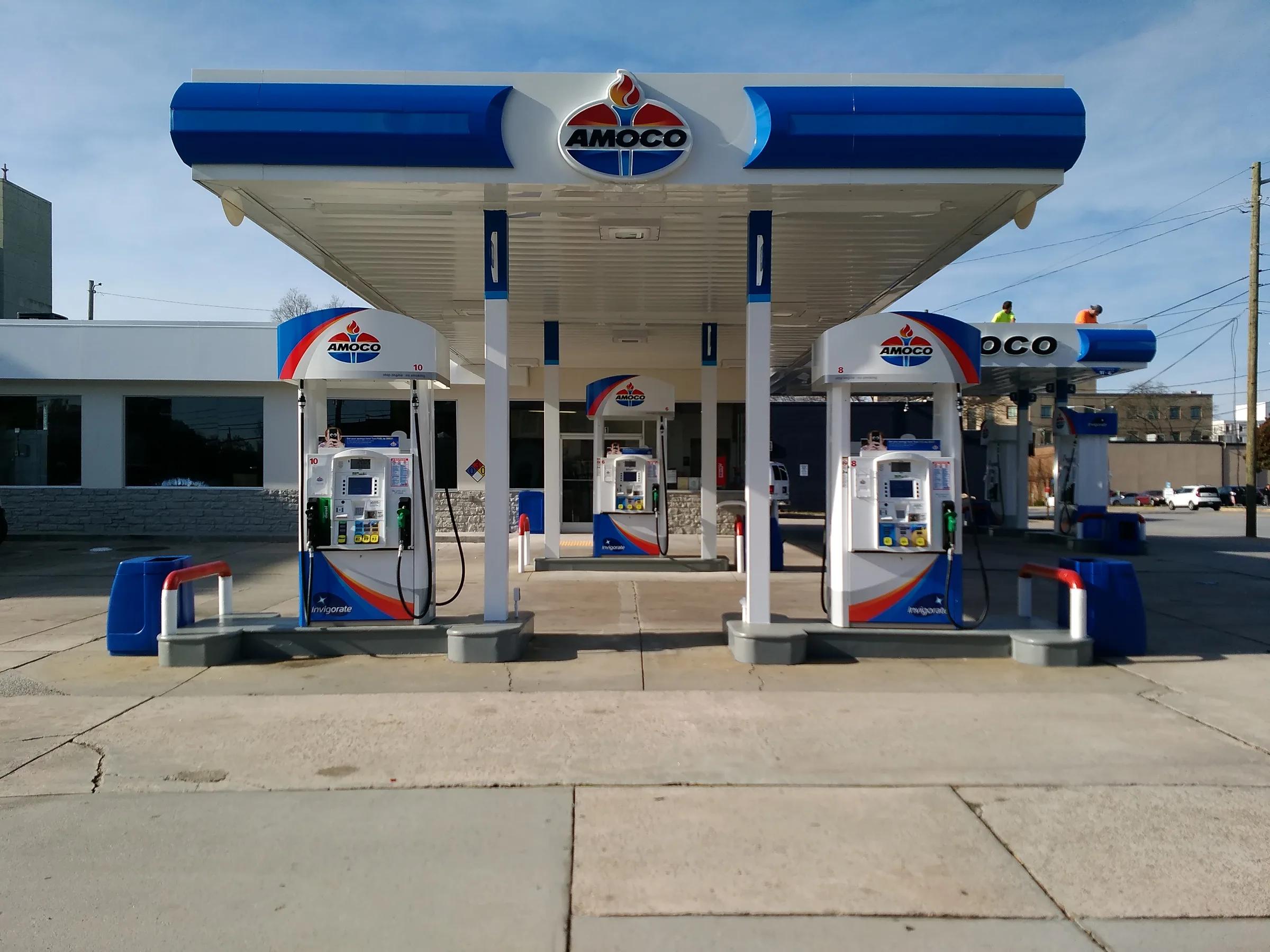 Amoco canopy and dispensers in blue, white and red, with two workers in safety vests on a second canopy behind