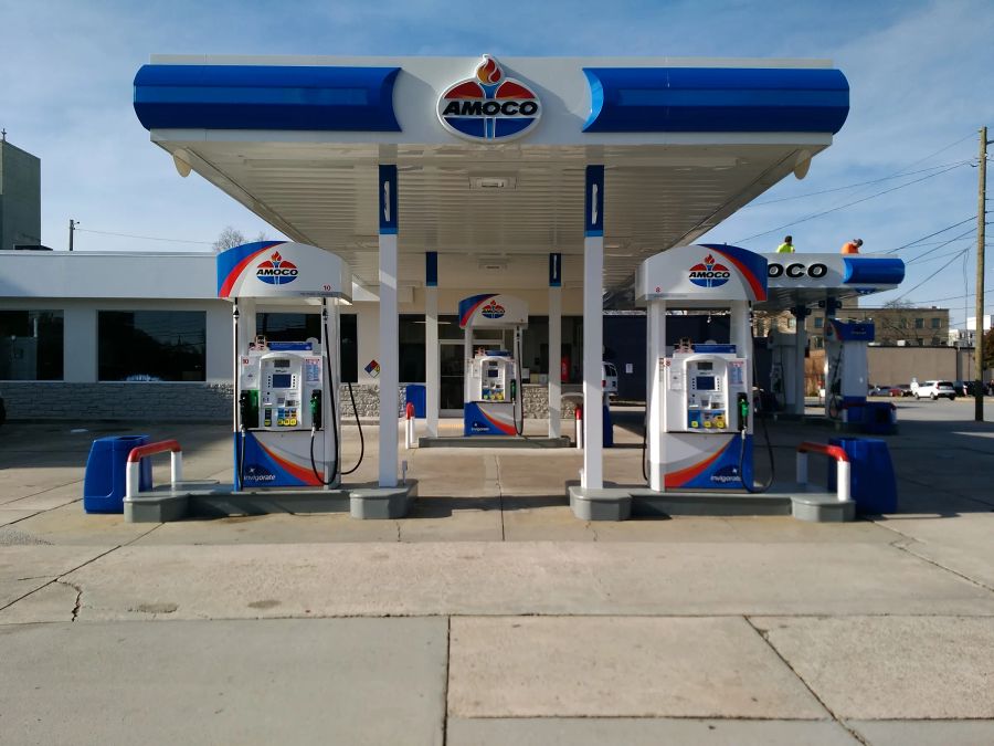 Amoco canopy and dispensers in blue, white and red, with two workers in safety vests on a second canopy behind
