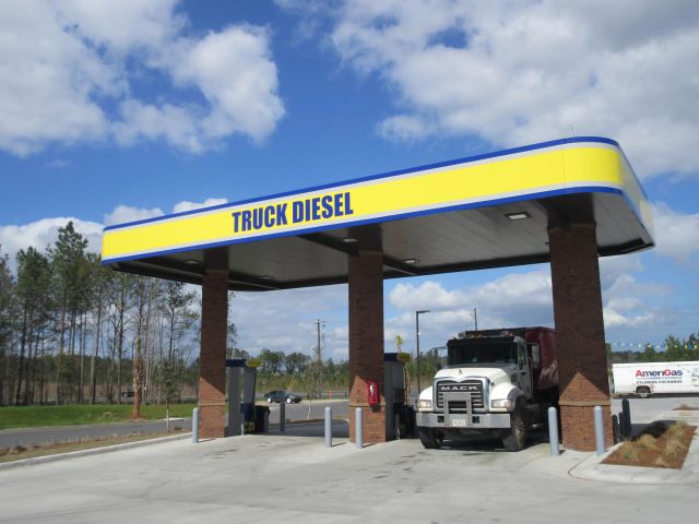 Truck diesel canopy with a yellow and blue fascia on brick columns, a dump truck at the pump