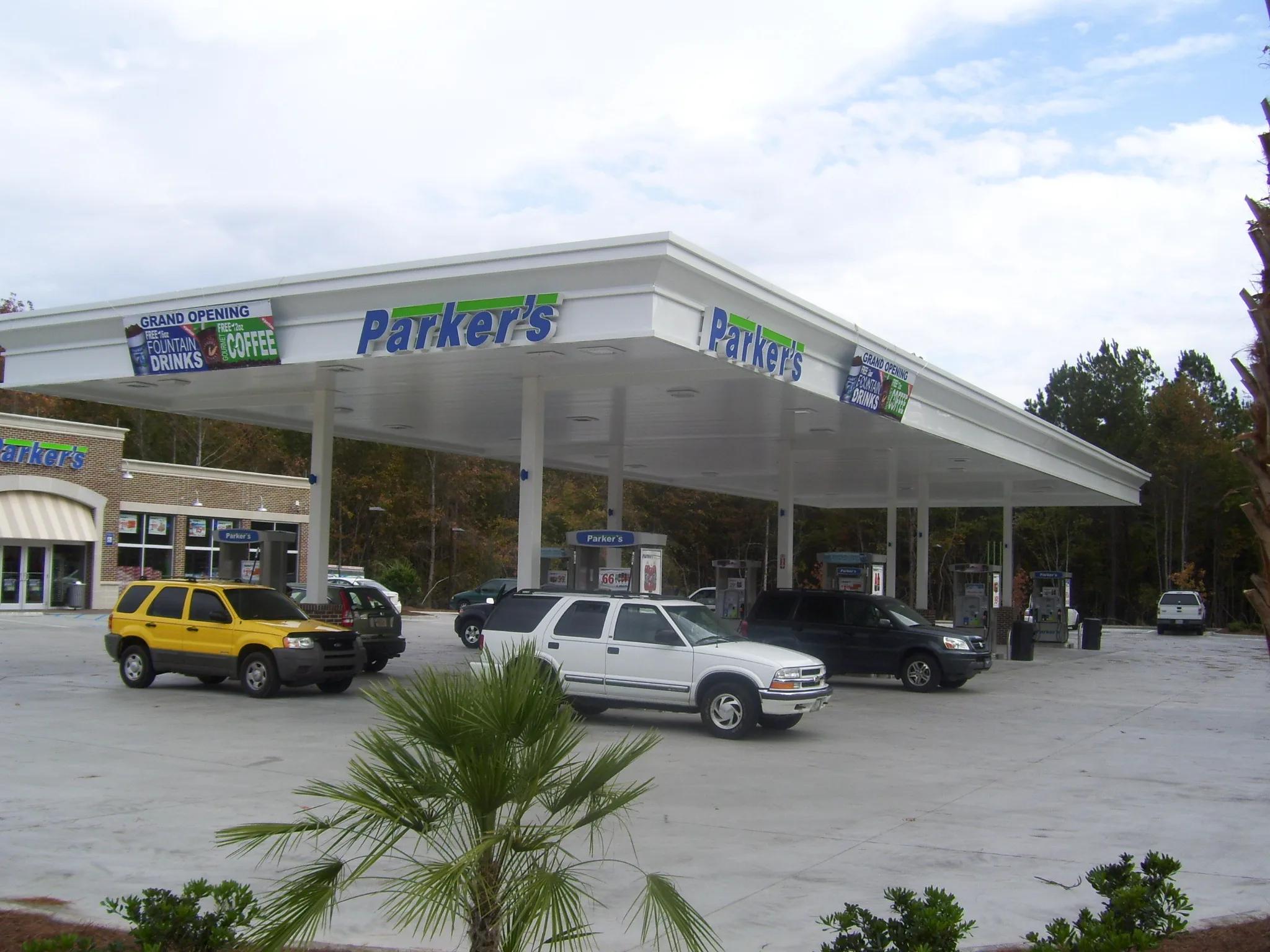 White canopy with store signs and grand opening banners over dispensers, cars at the pumps