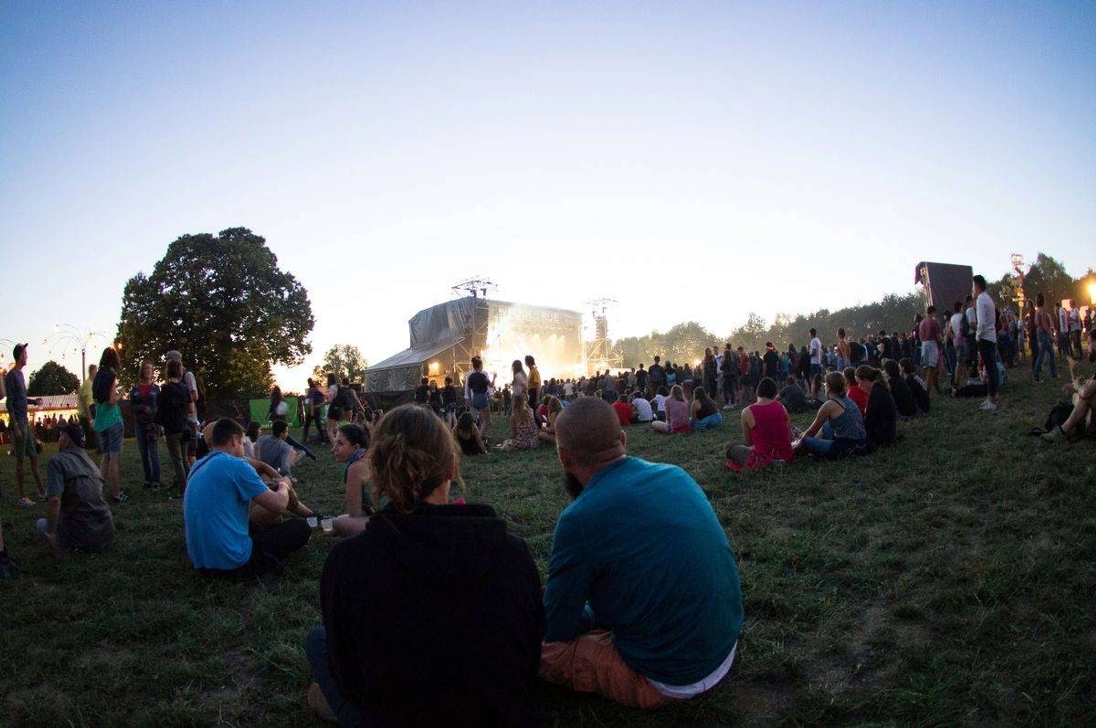Festivalpublik som sitter i gräset framför en scen i skymningen