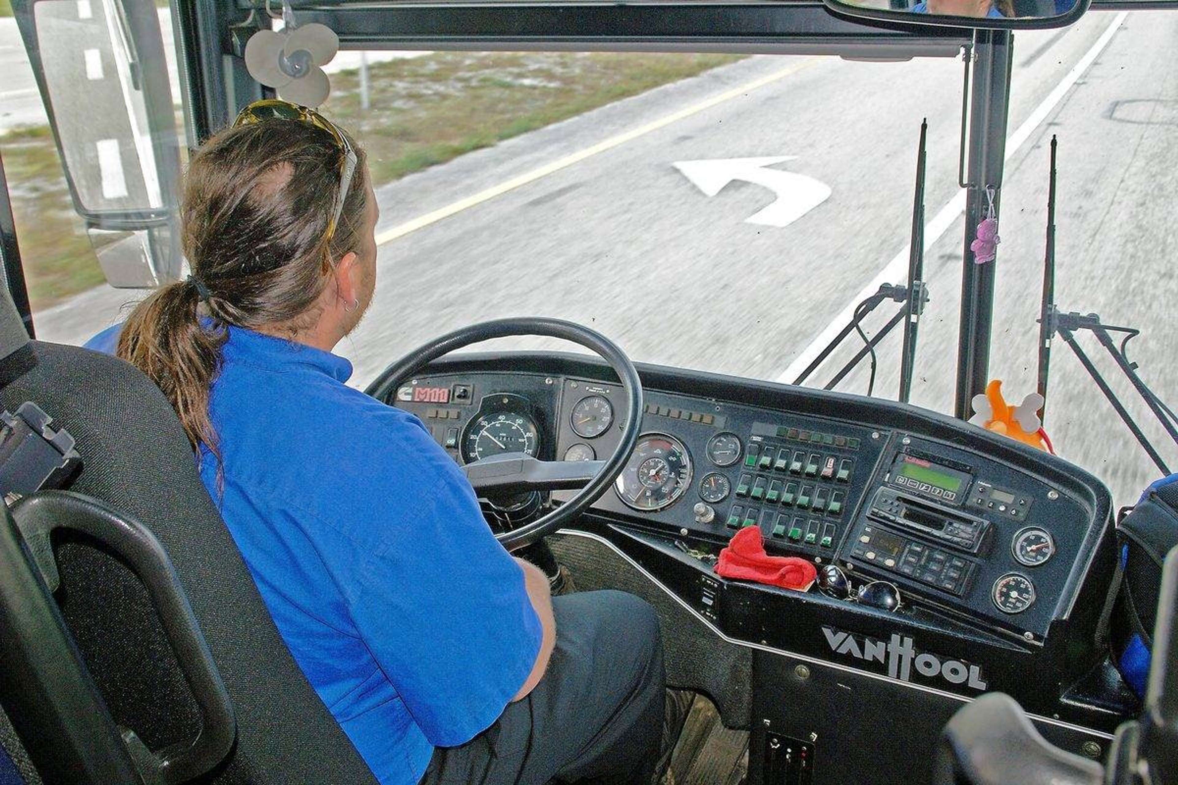 Busschaufför vid ratten i en turistbuss, sedd bakifrån med vägen framför