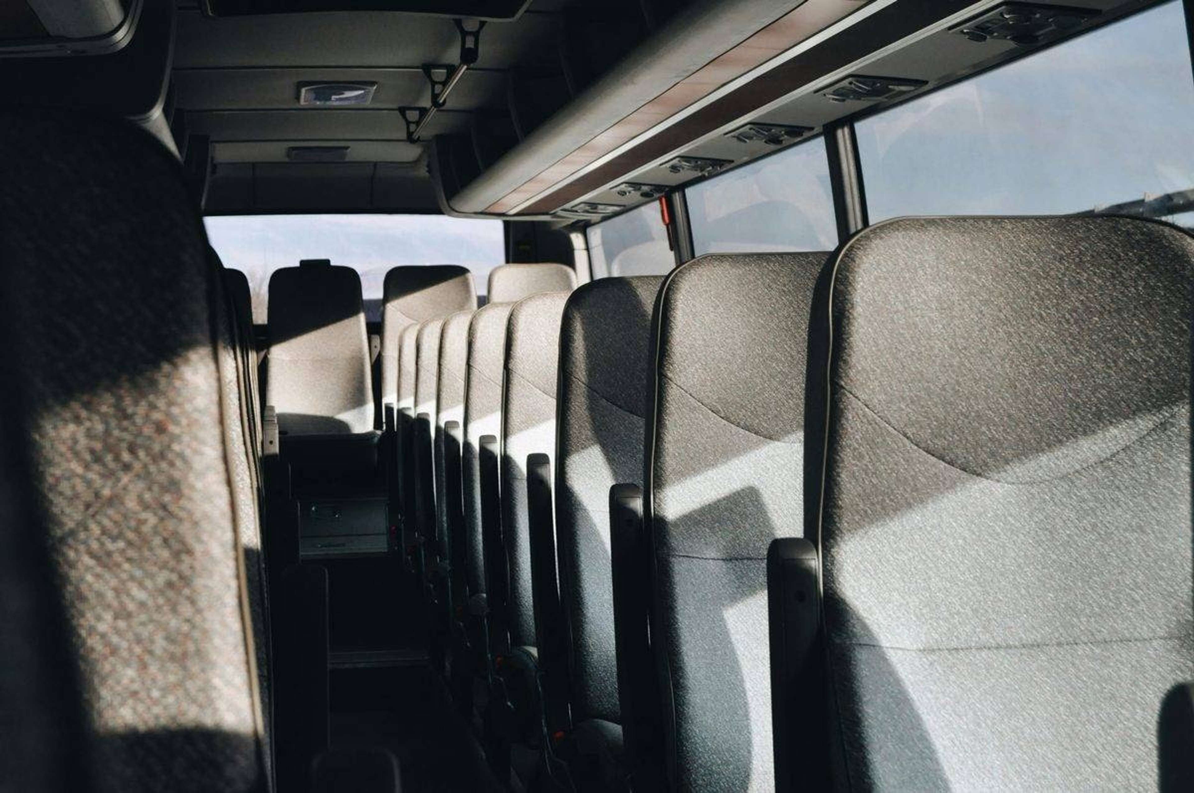 Tomma grå tygsäten i rader inne i en buss, med solljus som faller in genom fönstren