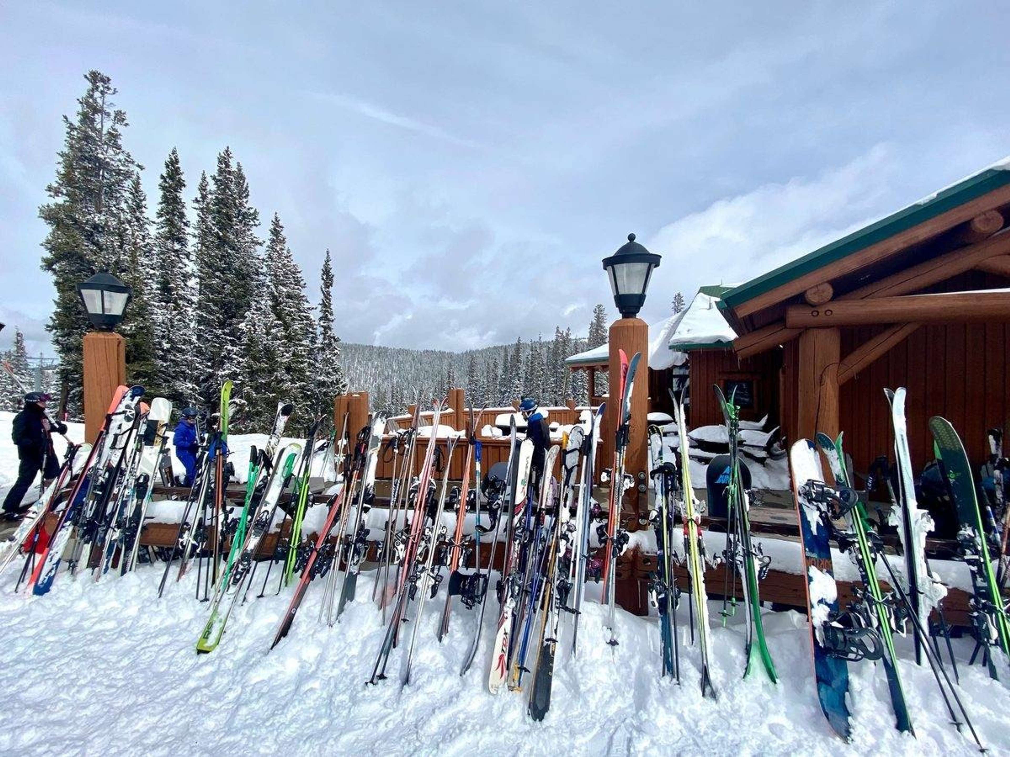 Ski og staver stilt opp i snøen utenfor en tømmerhytte i skianlegget