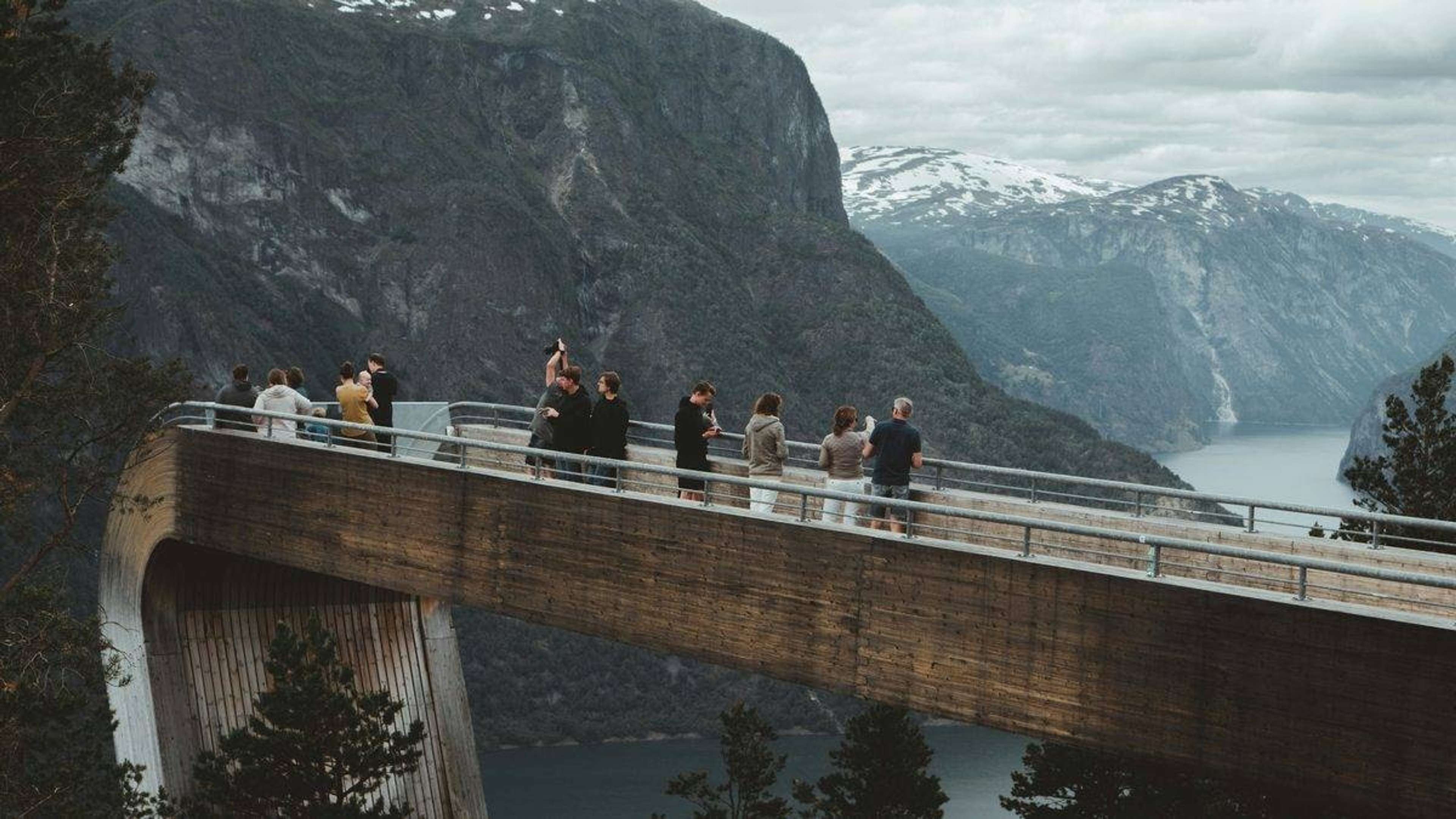 Gruppe mennesker på en utsiktsplattform over en fjord med bratte fjellsider