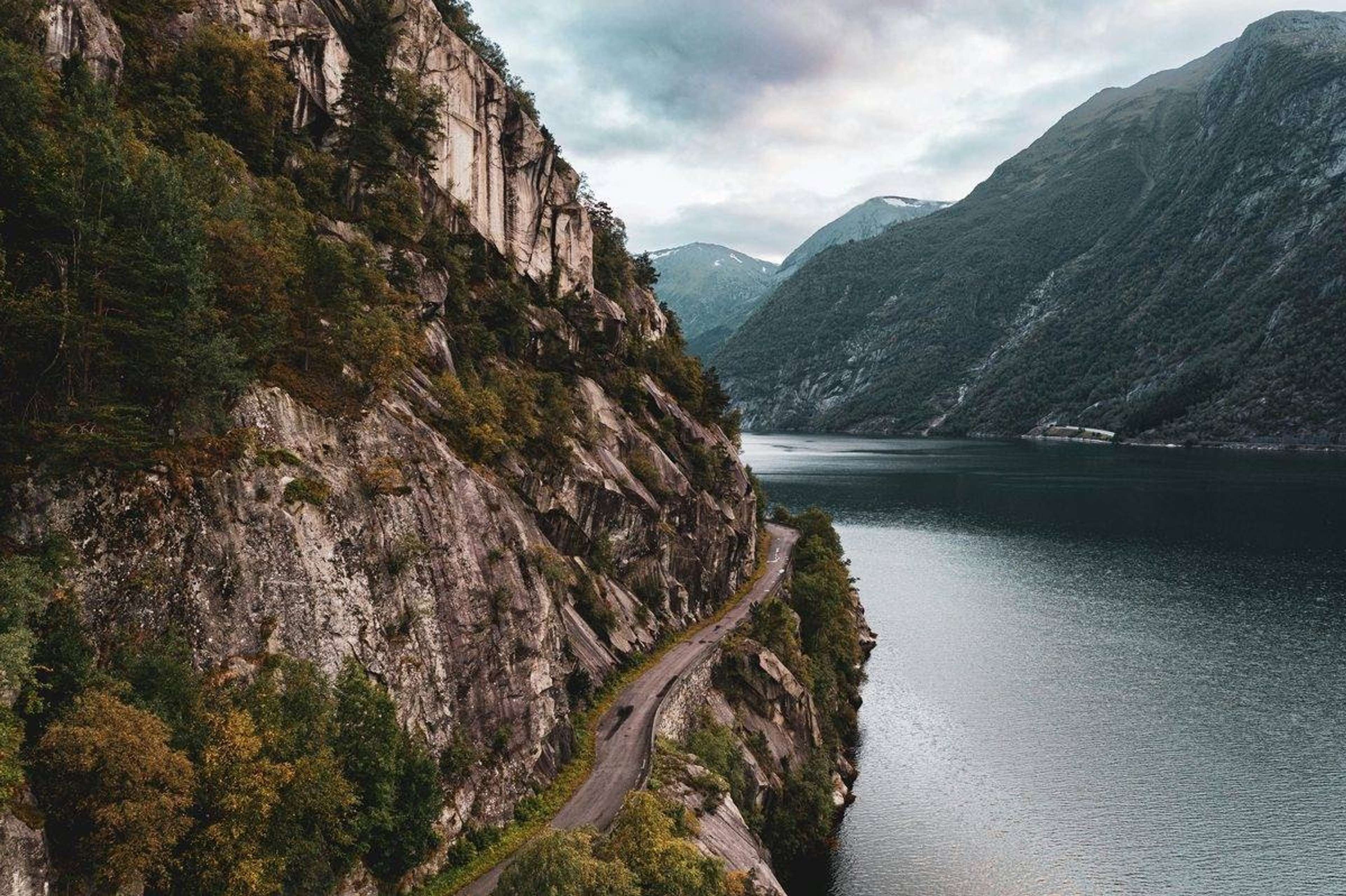 Smal vei langs en bratt fjellside over en fjord, med fjell i bakgrunnen