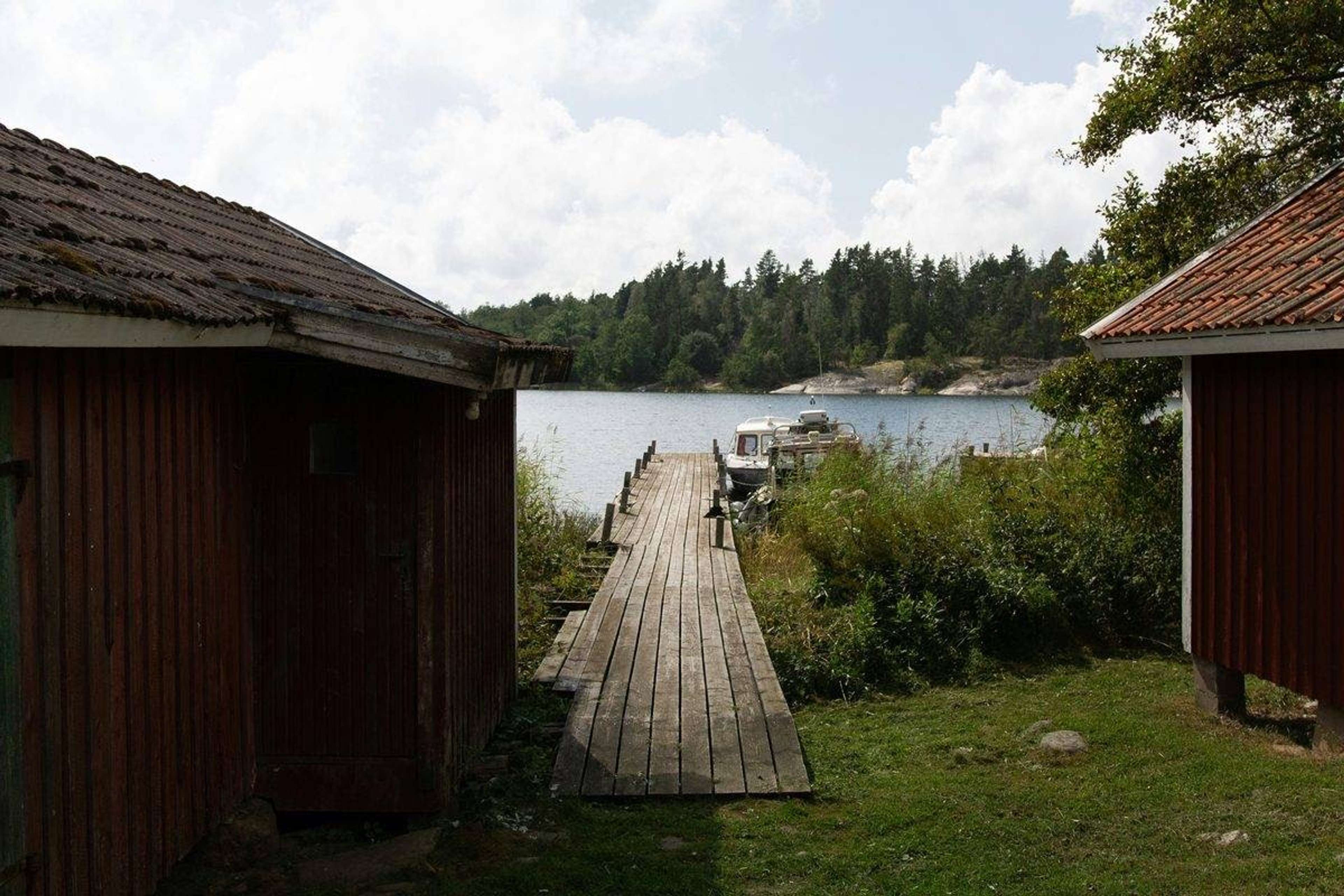 Træbro mellem to røde bådehuse ud mod vandet en sommerdag