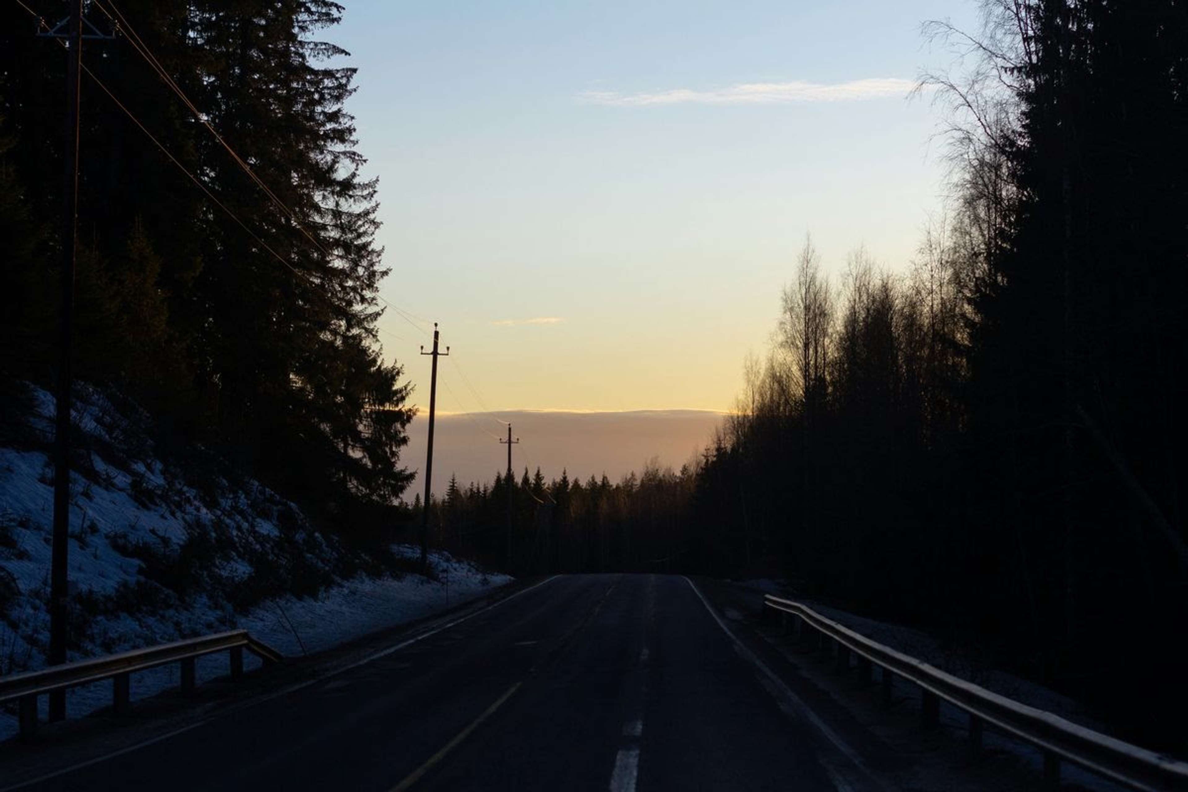 Talvinen maantie havumetsän halki auringonlaskussa, tien reunoilla lunta