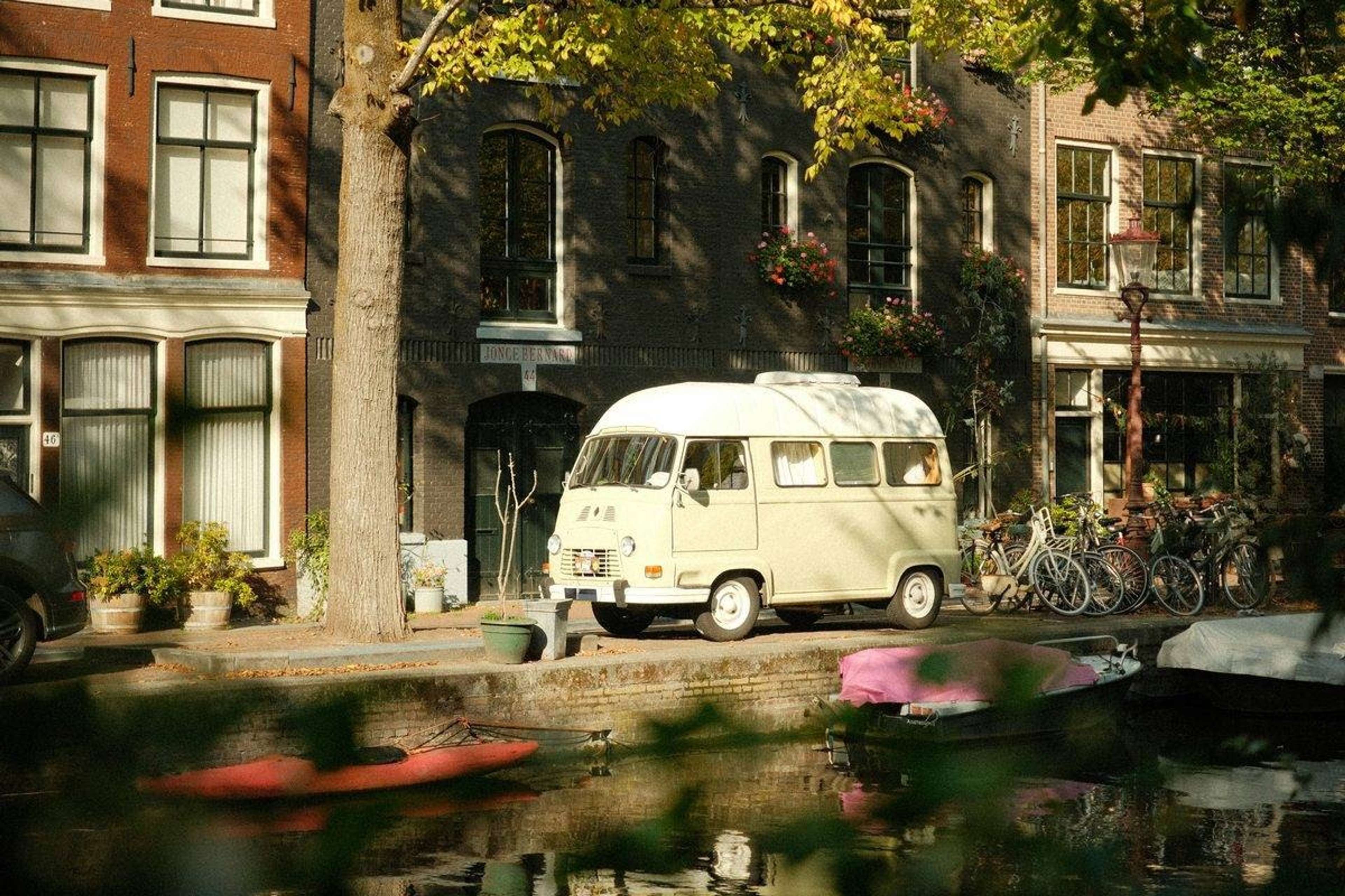 Gammel cremefarvet minibus parkeret ved en kanal foran murstenshuse og cykler