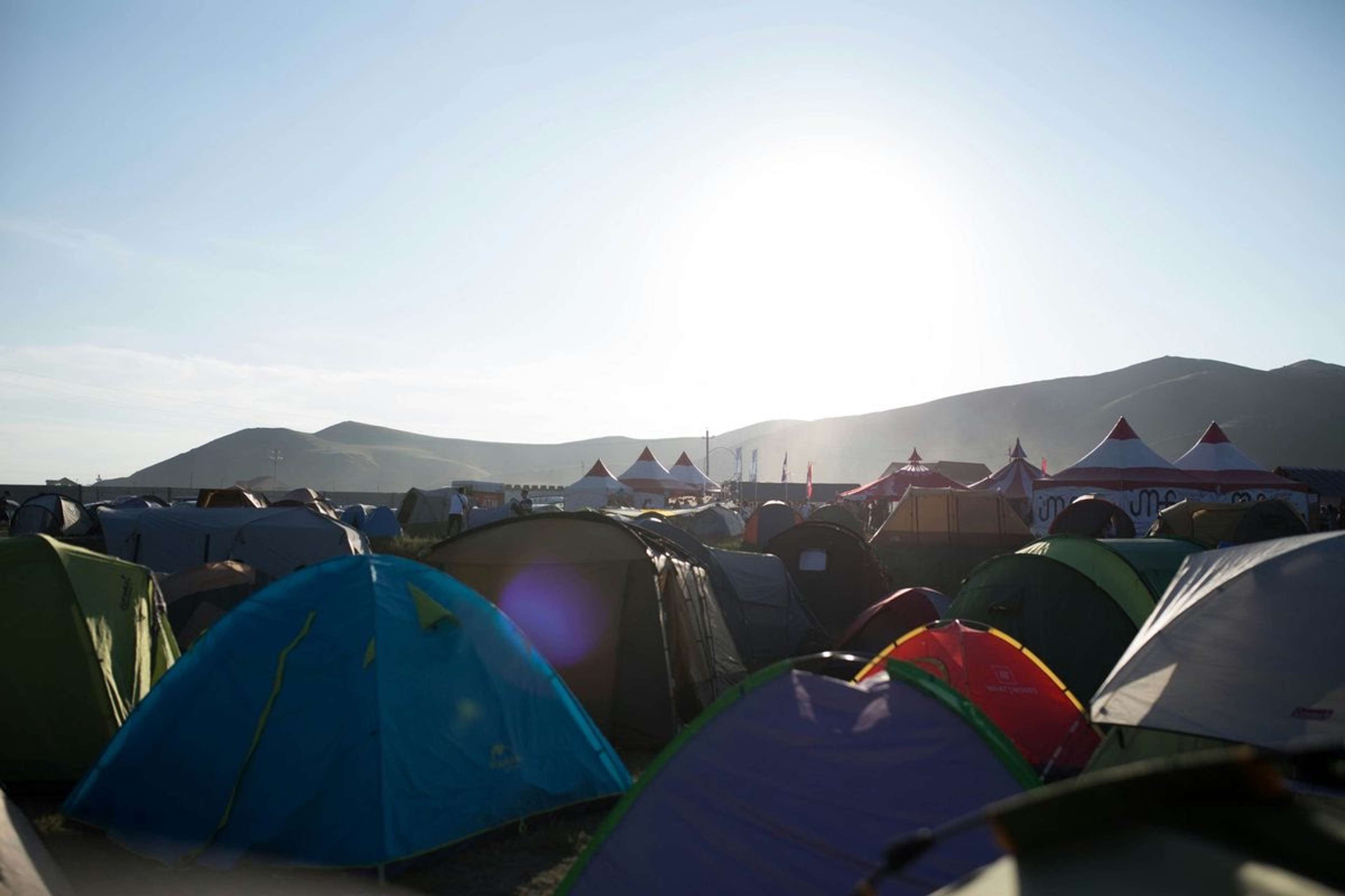 Farverige telte på en festivalcampingplads med bakker i baggrunden i modlys