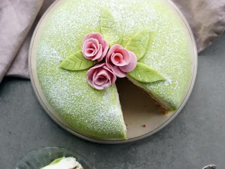 Prinsesstårta sedd ovanifrån, täckt med grön marsipan, dekorerad med en rosa marsipanros och ett tunt lager florsocker.