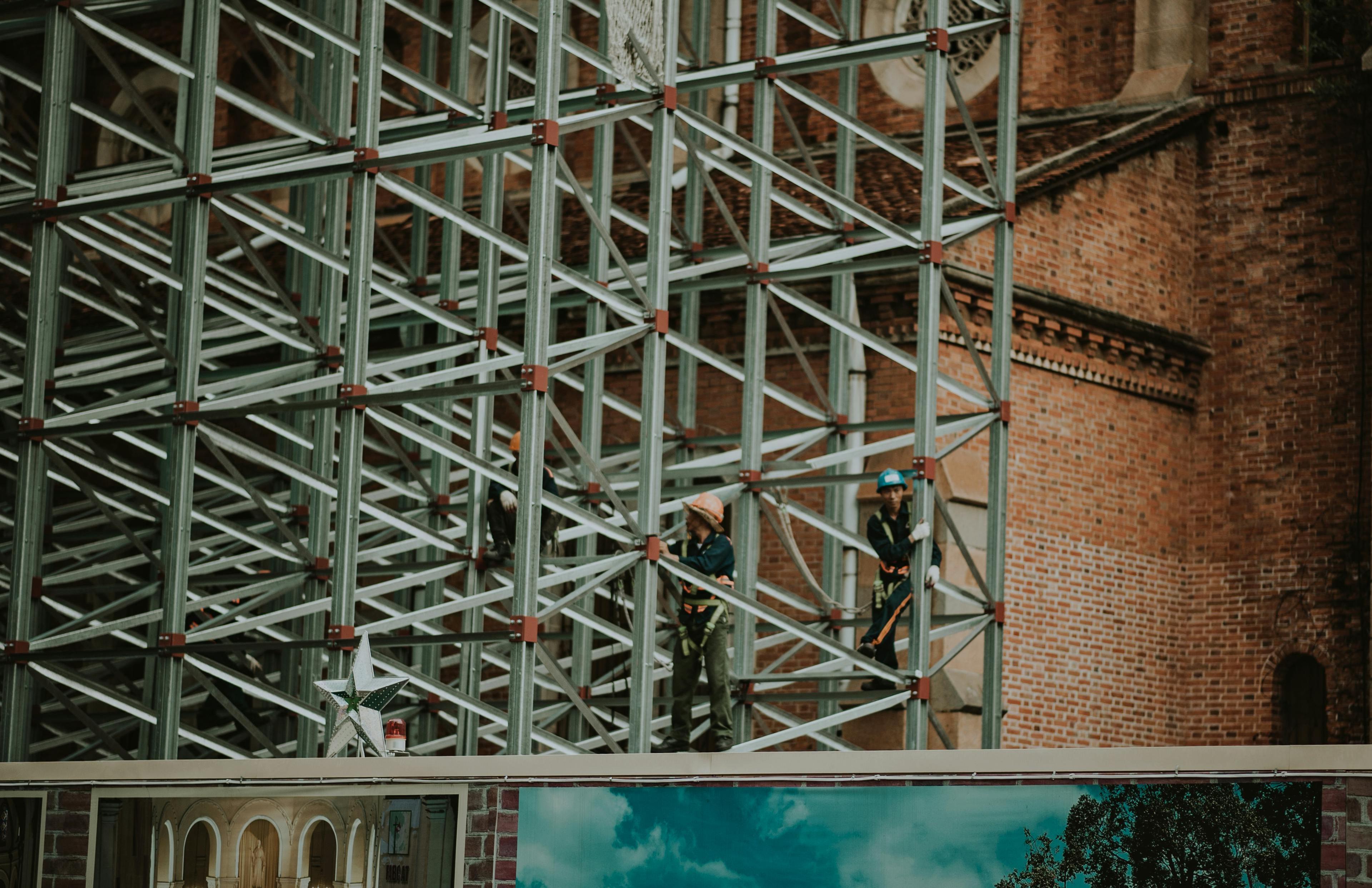 two people in work clothes on the side of a red brick building undergoing construction