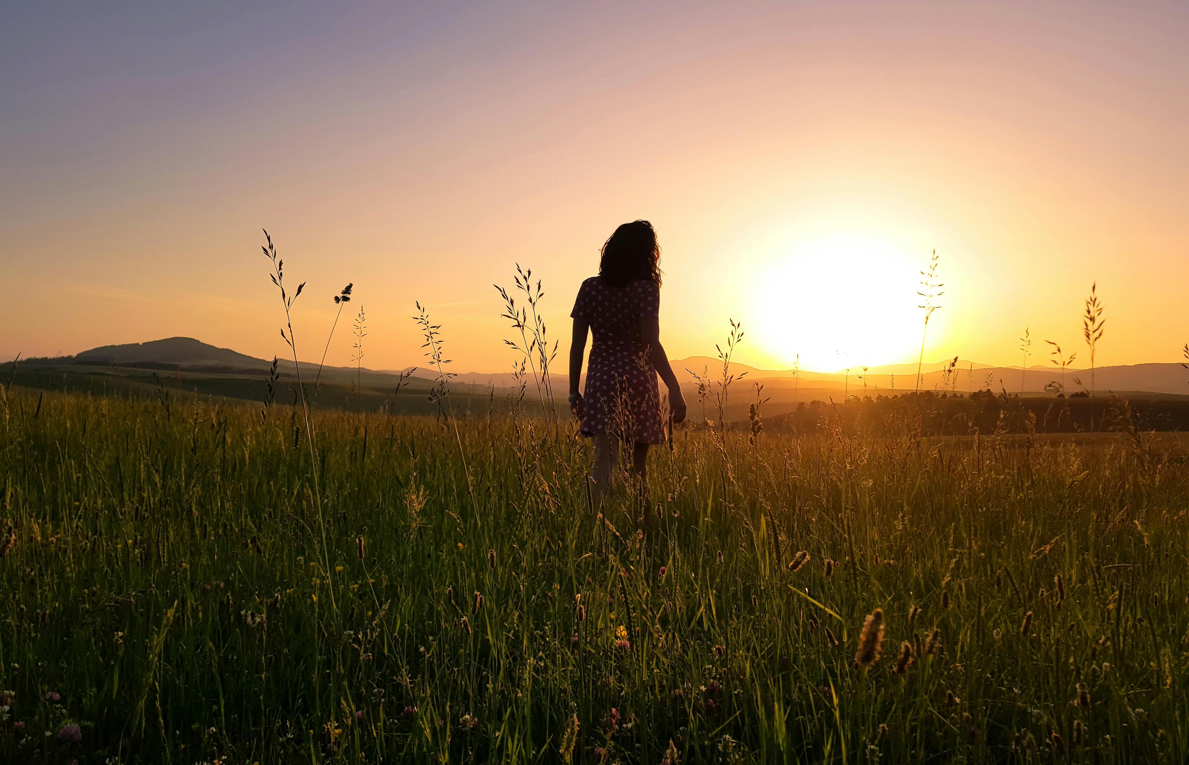 Woman standing in green field at sunset