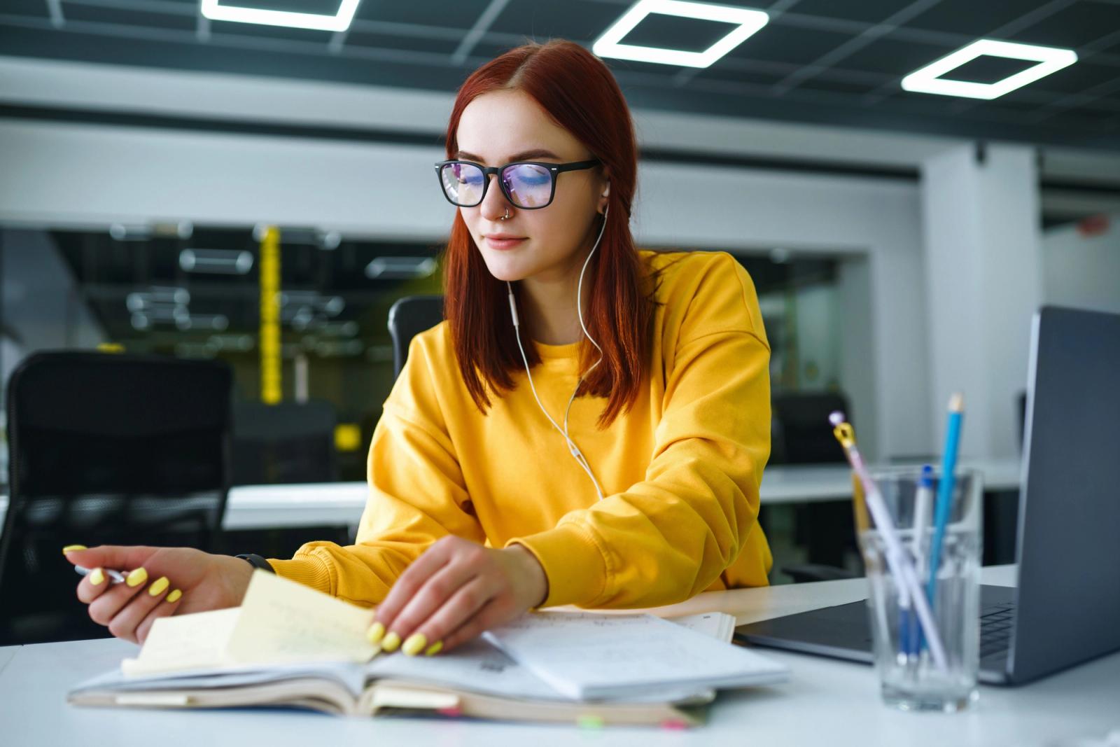 Young woman wearing yellow sits at a computer in an office environment