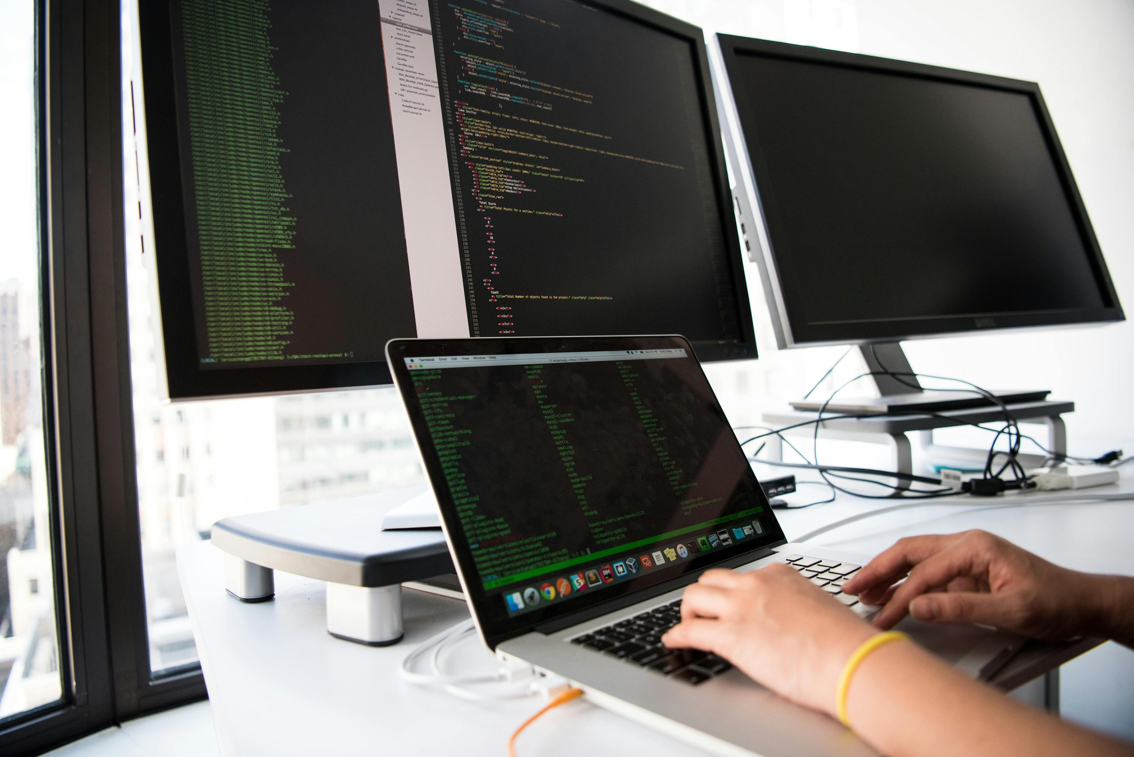 White person's hands typing code on a laptop that is connected to an external monitor