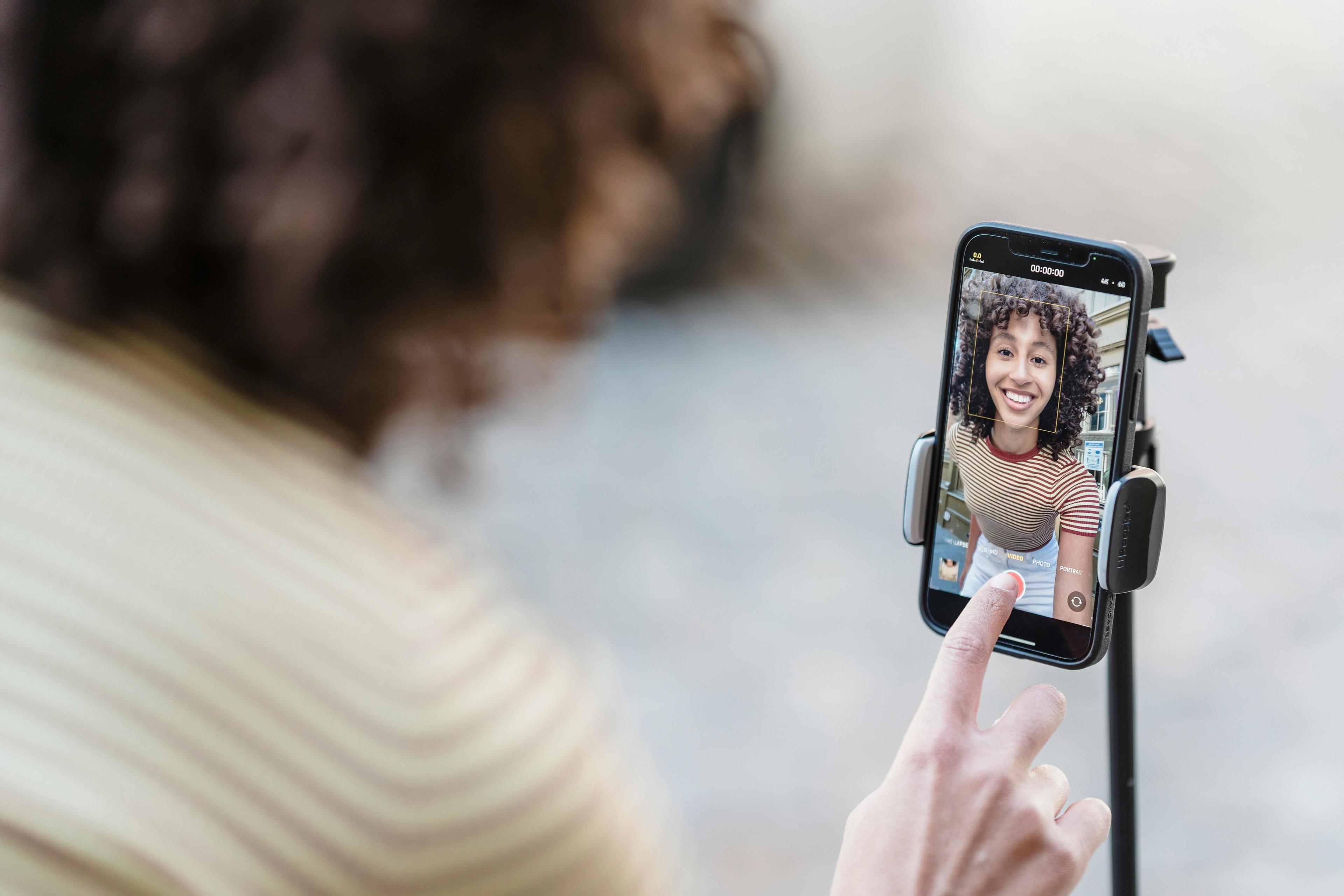 happy young woman using a tripod to film a video on an iPhone