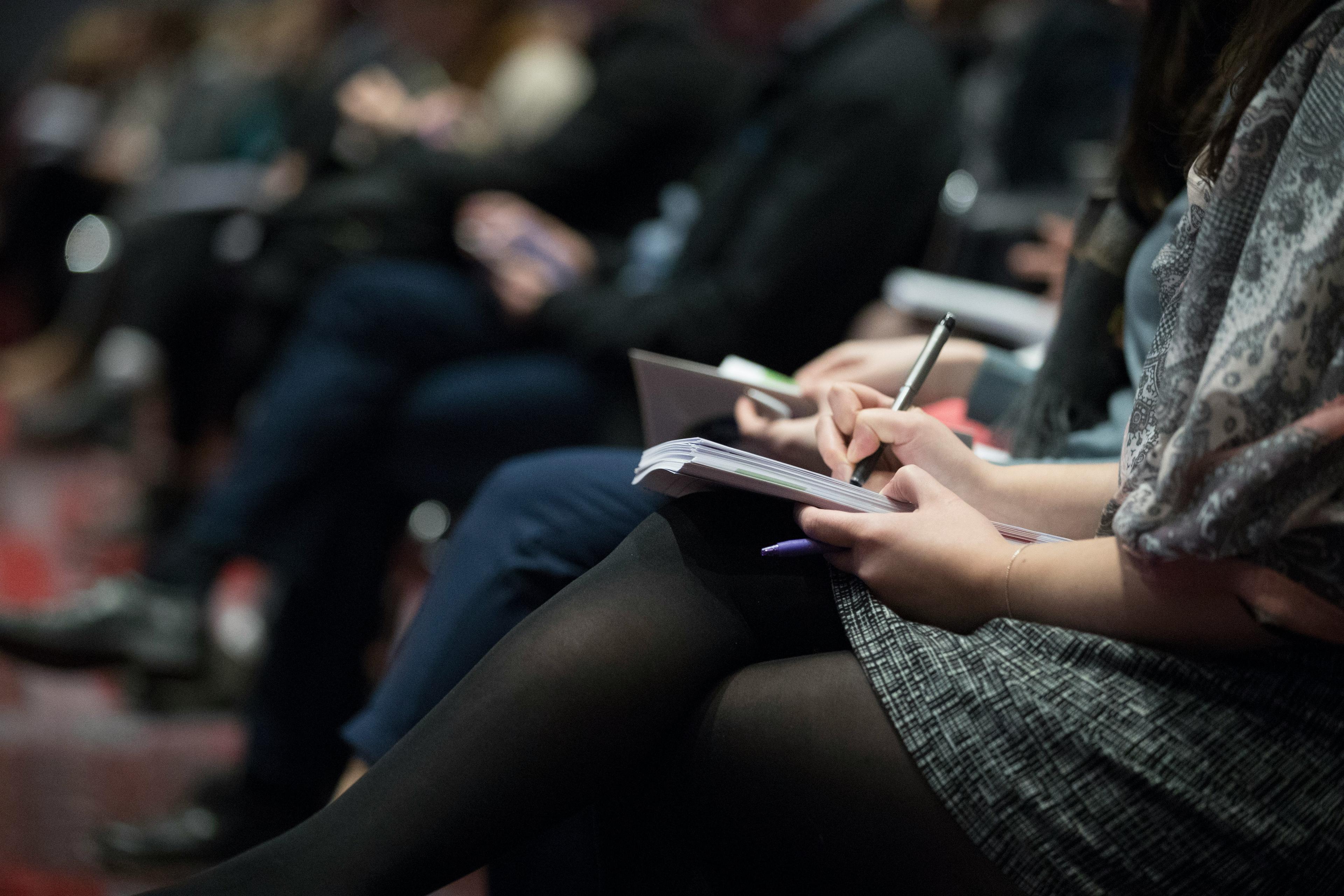 person's torso sitting with legs crossed in a lecture taking notes