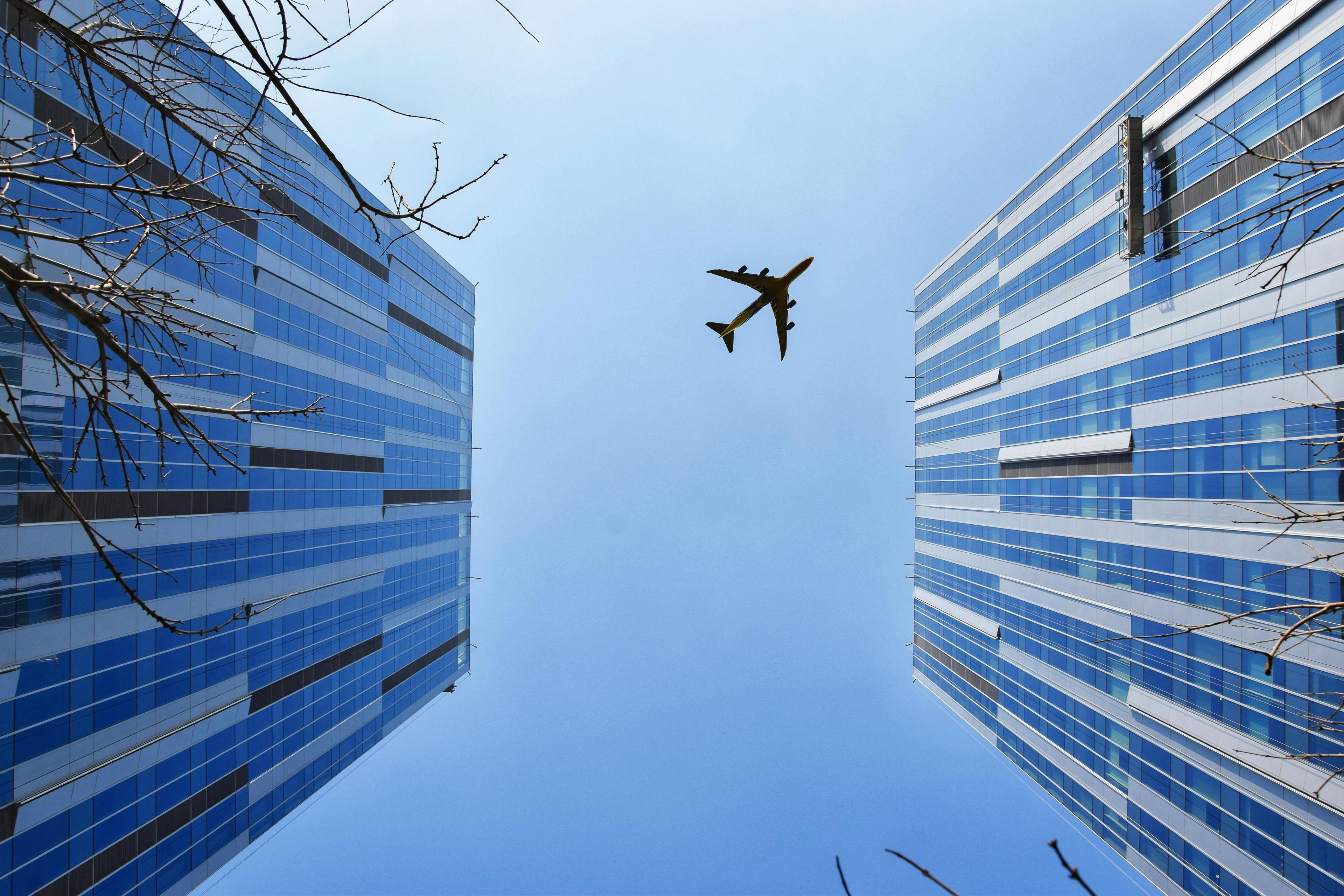 A view of two buildings and an airplane from beneath with blue sky in the background.