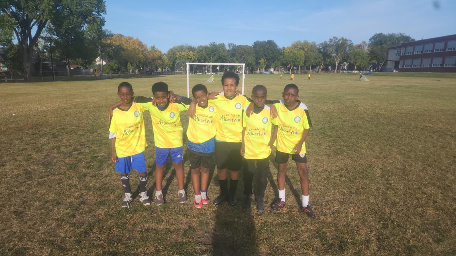 Six boys in yellow SISSA youth soccer jerseys pose together on a grass soccer field.