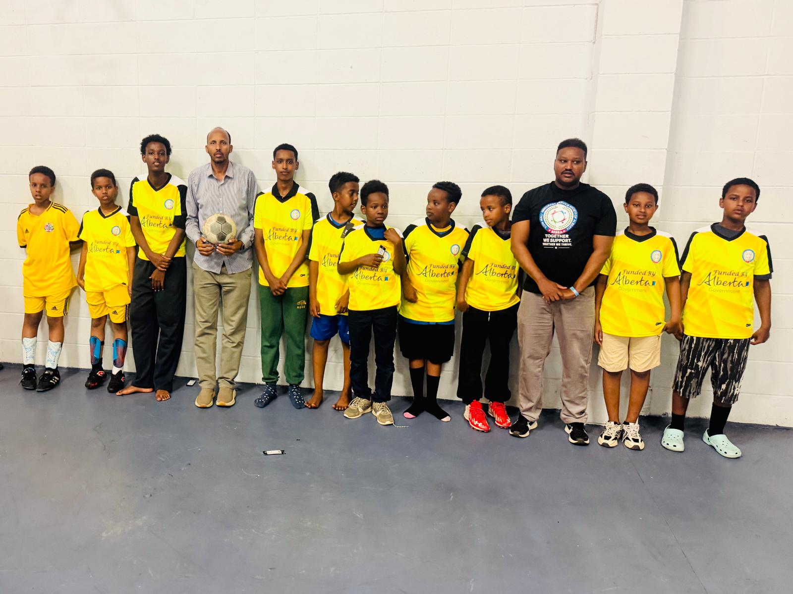 SISSA youth soccer team in yellow Alberta-funded jerseys poses with two coaches.