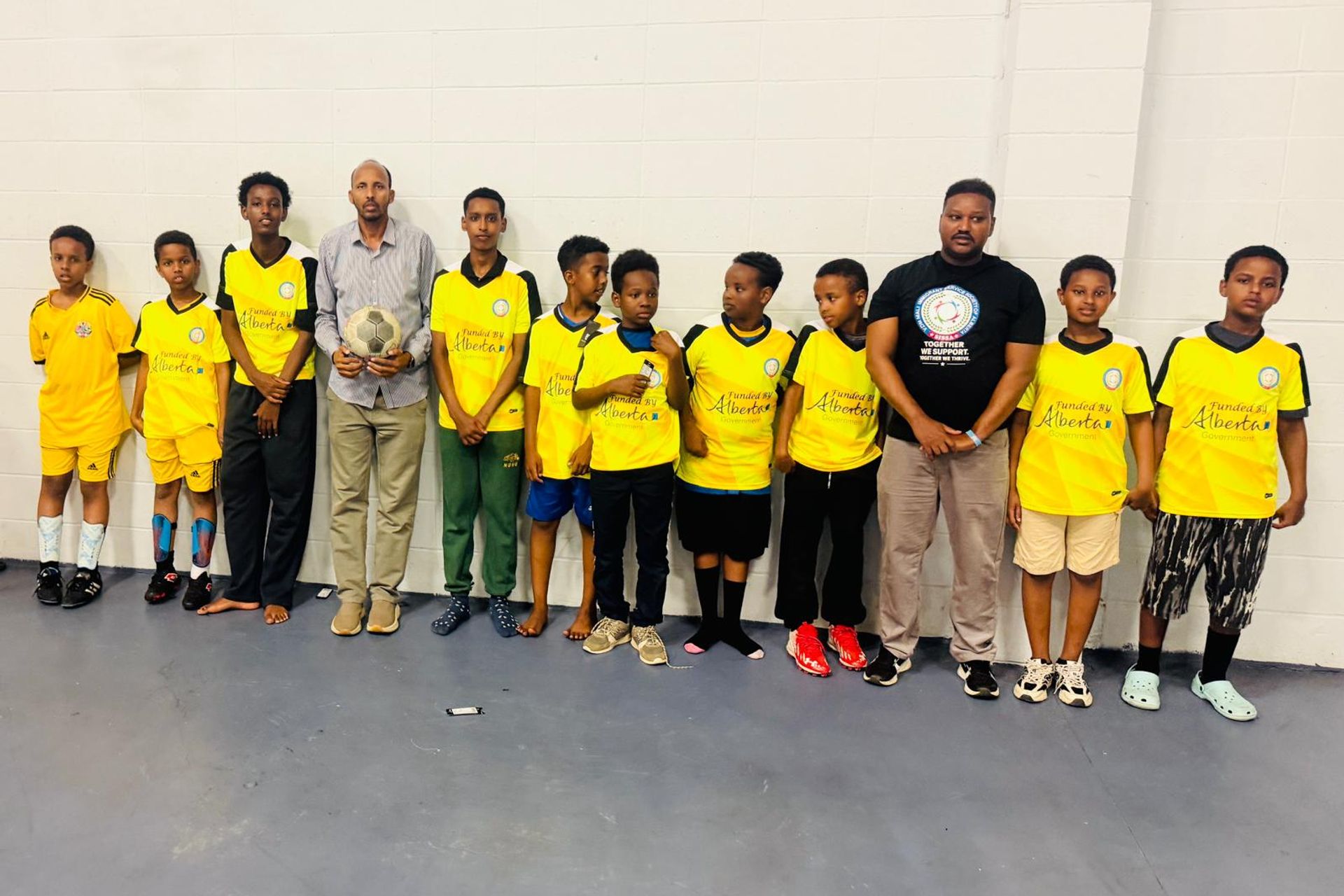 SISSA youth soccer team in yellow Alberta-funded jerseys poses with two coaches.