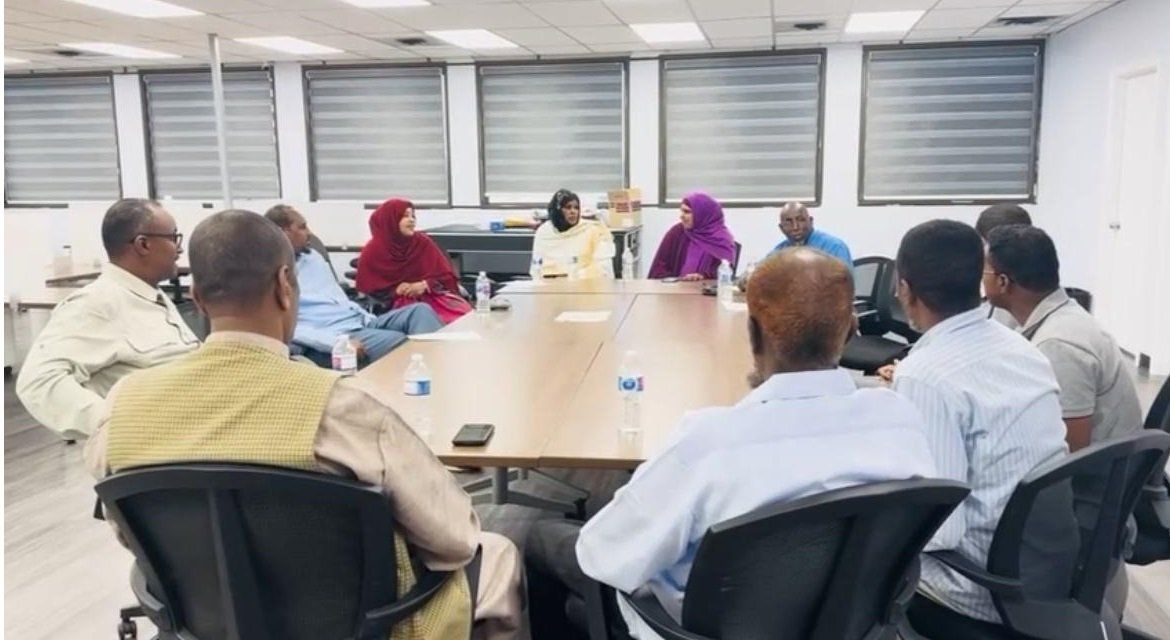 Community members sit around a conference table in a bright meeting room, talking together.