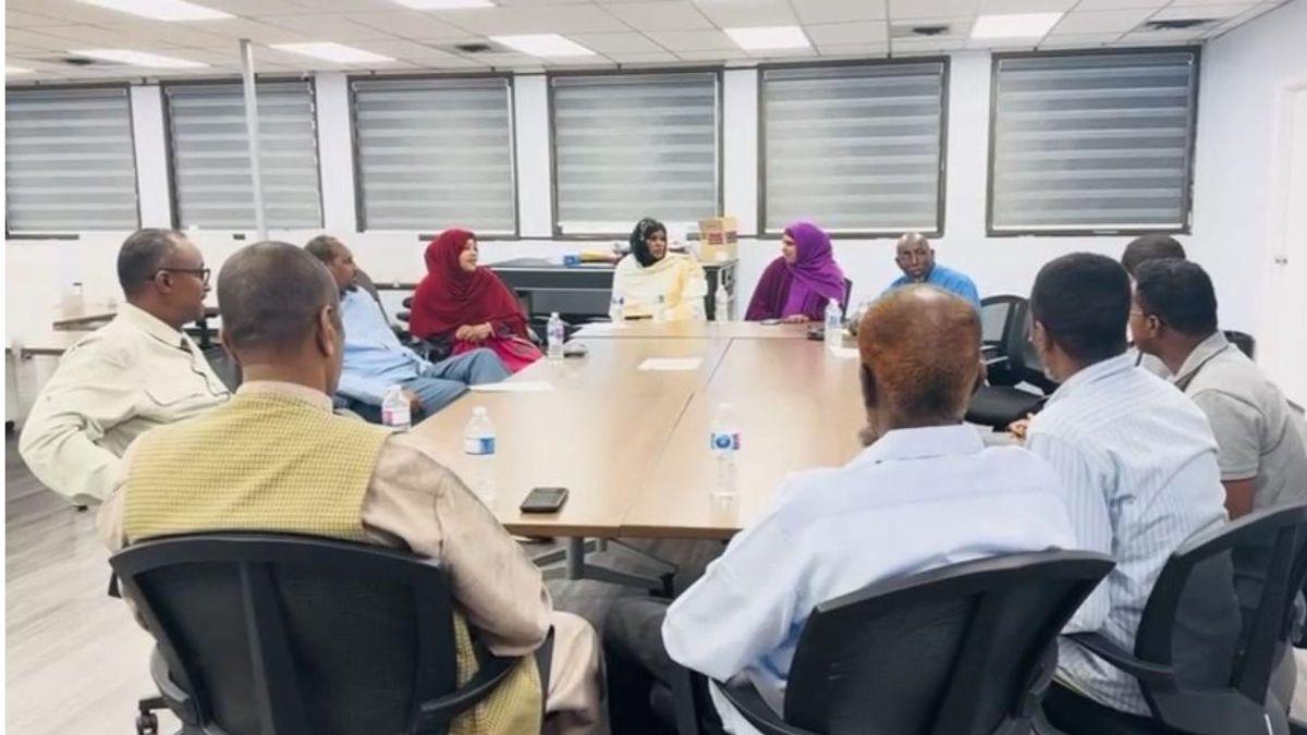 Community members sit around a conference table in a bright meeting room, talking together.