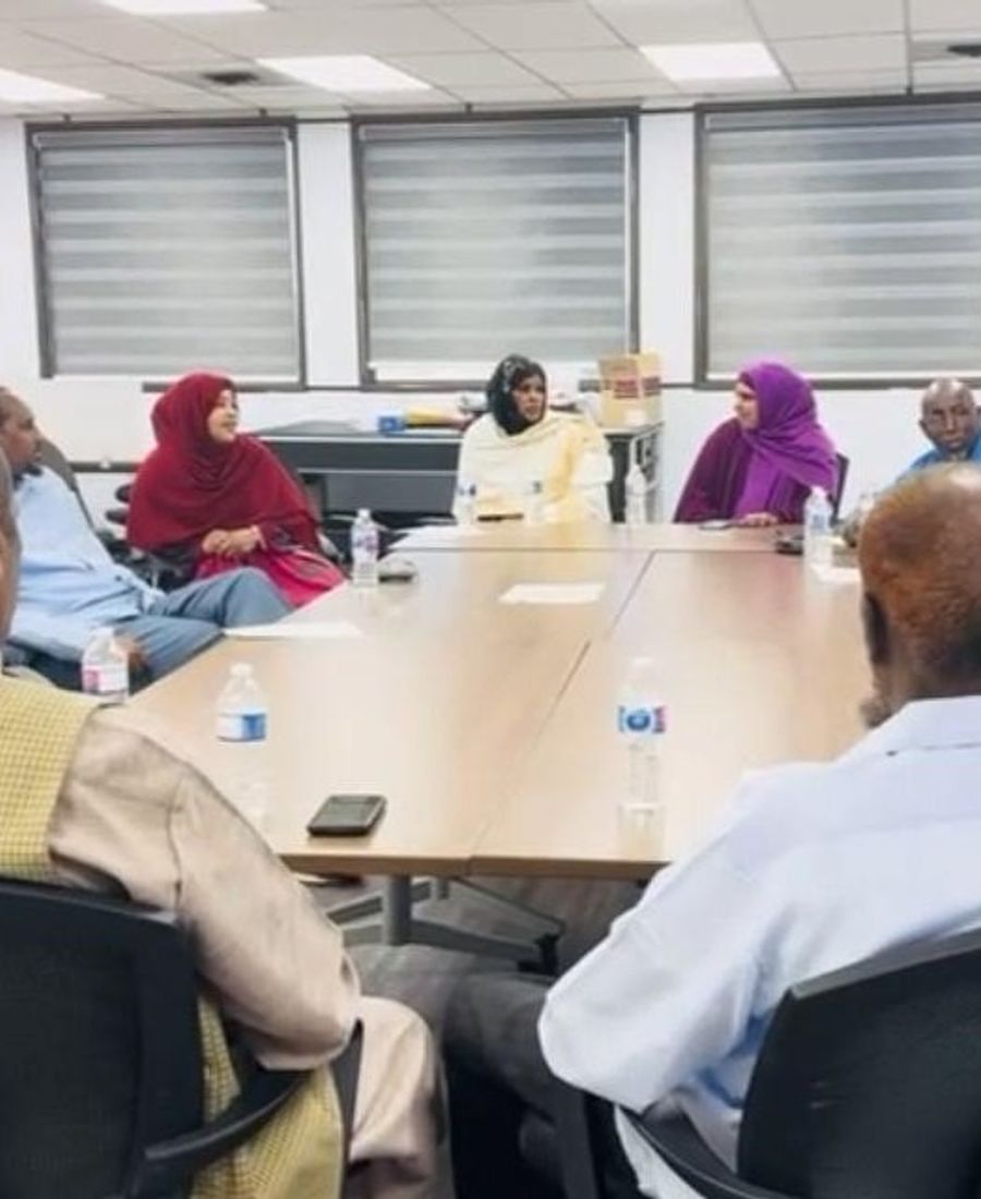 Community members sit around a conference table in a bright meeting room, talking together.