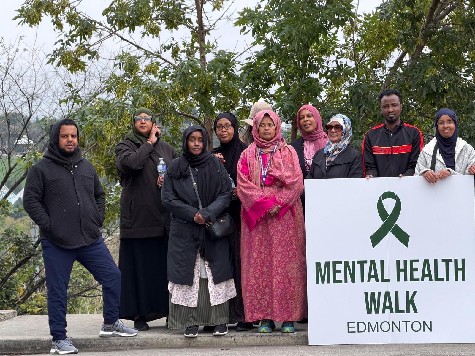 Community members pose outdoors holding a Mental Health Walk Edmonton sign.