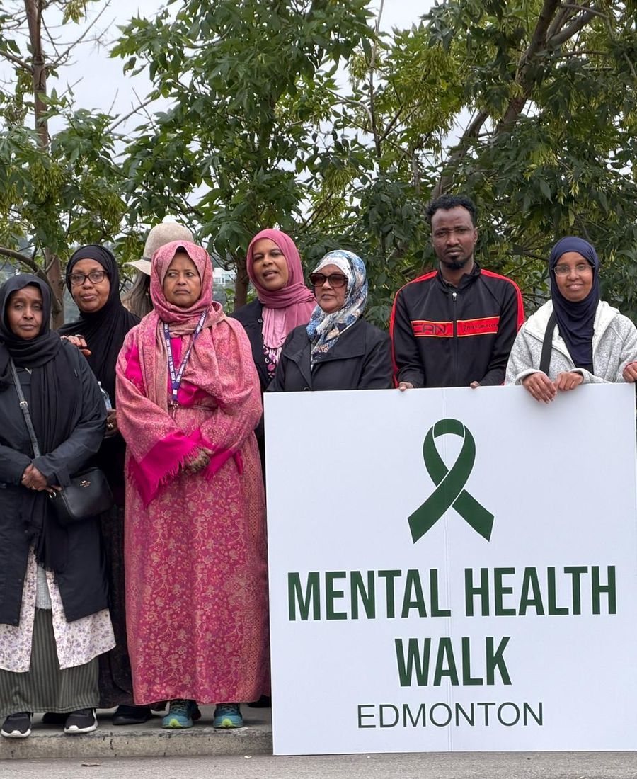 Community members pose outdoors holding a Mental Health Walk Edmonton sign.
