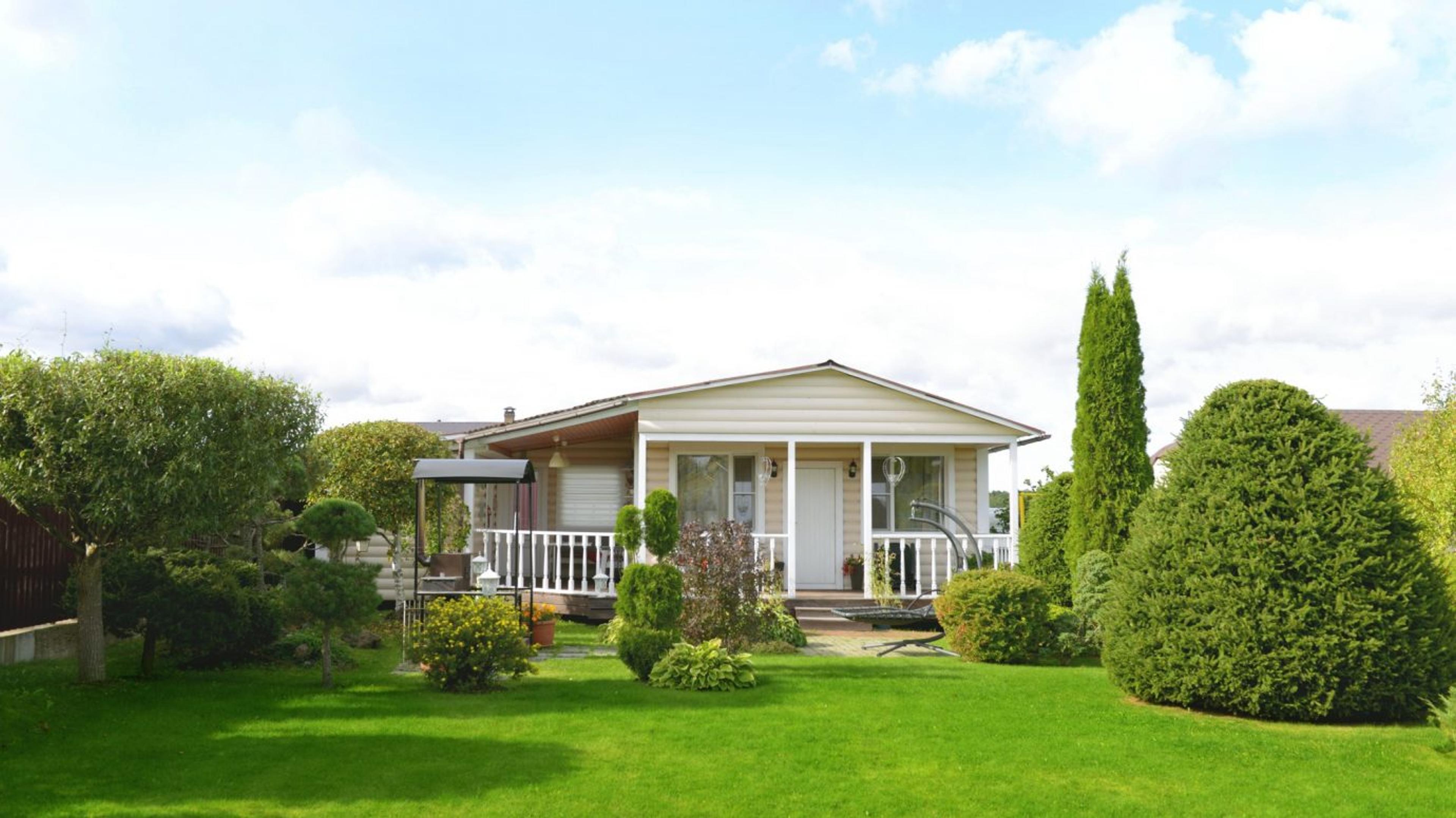 A well maintained yard with sculpted evergreen shrubs, layered foundation plantings, and a lush trimmed lawn framing the front porch, showcasing the property at its best.