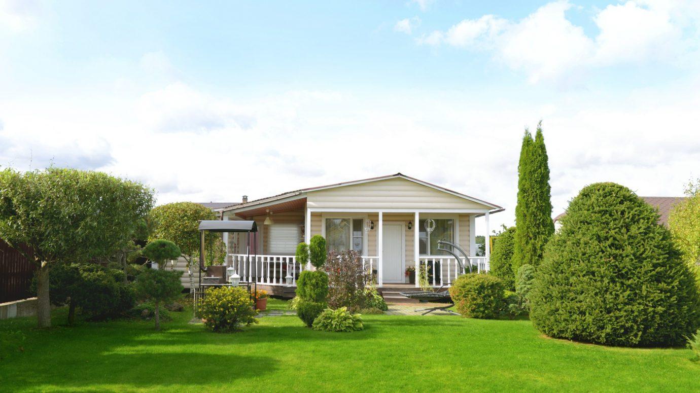 A well maintained yard with sculpted evergreen shrubs, layered foundation plantings, and a lush trimmed lawn framing the front porch, showcasing the property at its best.