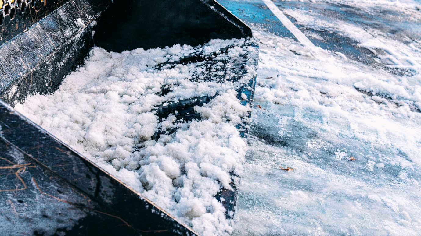 A snowplow collects snow from an icy, snowy parking lot, clearing paths and ensuring safe parking for vehicles.