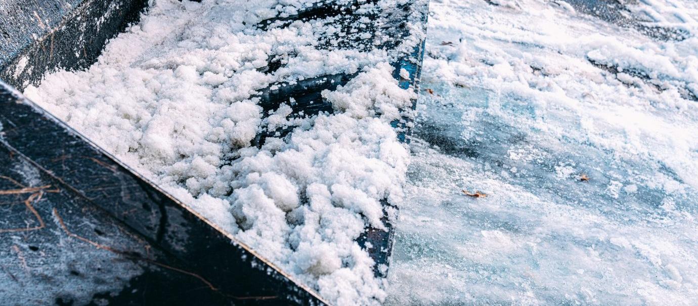A snowplow collects snow from an icy, snowy parking lot, clearing paths and ensuring safe parking for vehicles.