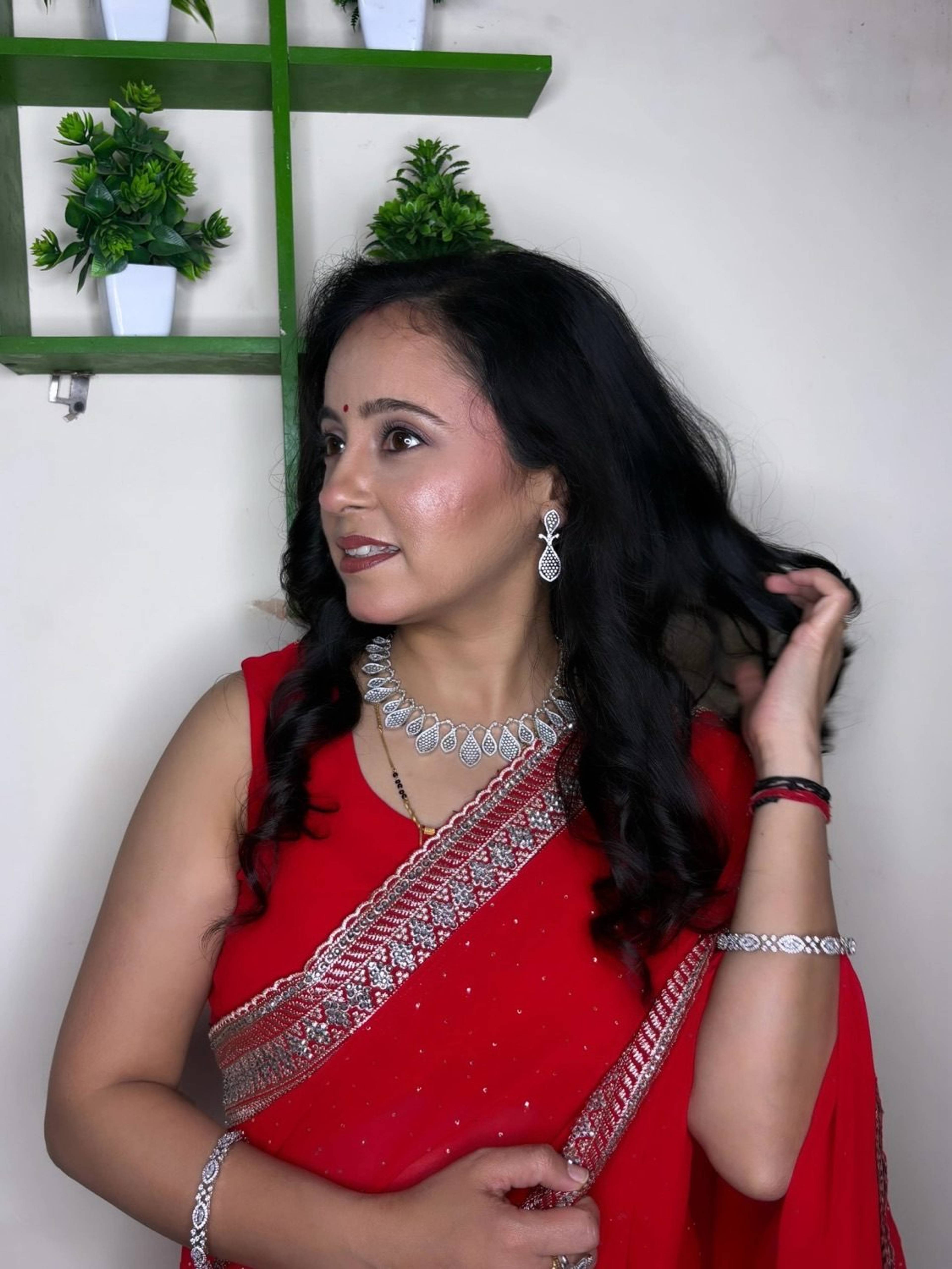 Party makeup with dewy skin and defined eyes paired with a red saree, by Priya Maleri