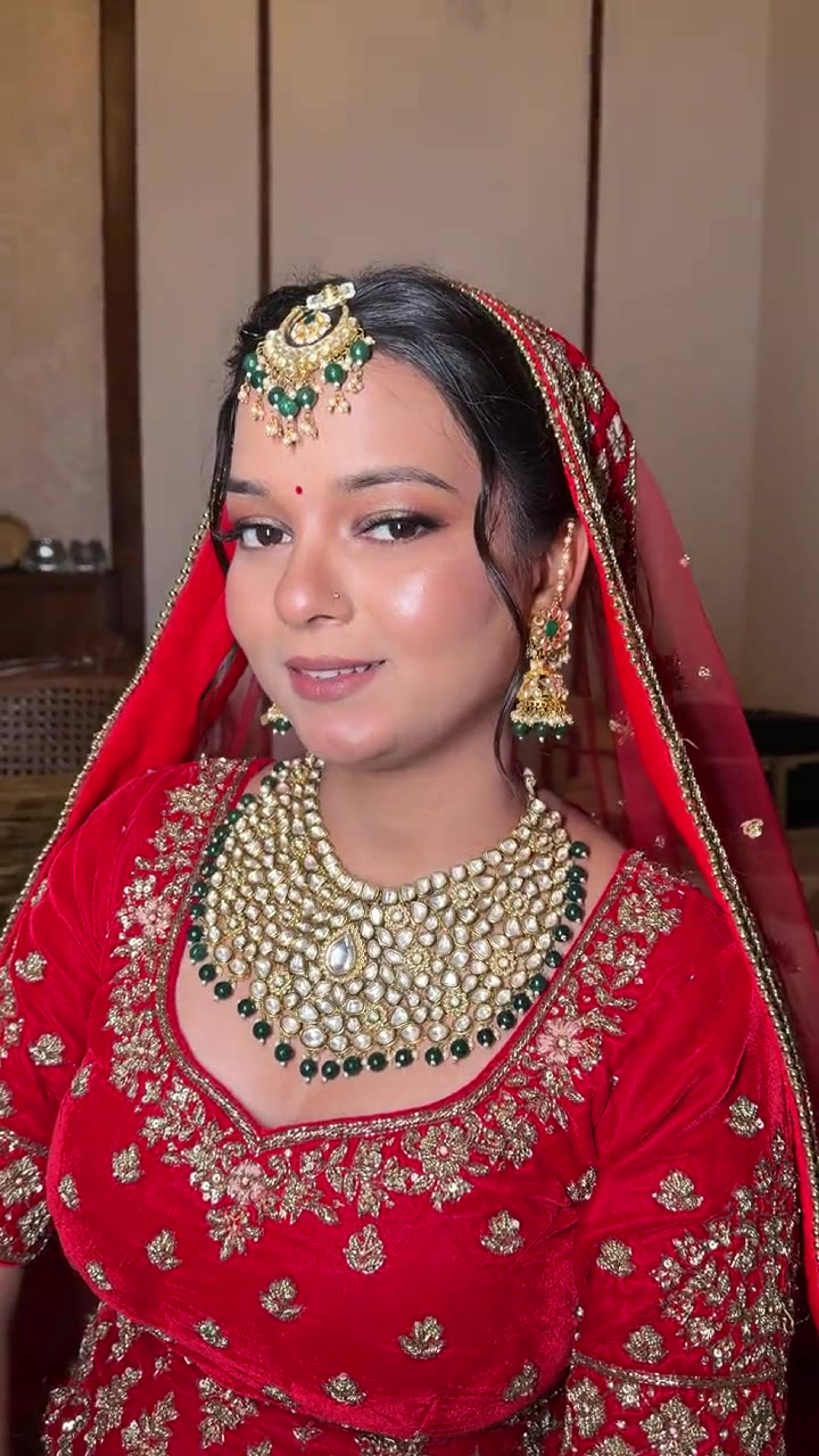 Video reel of a bride in a red embroidered lehenga with kundan jewellery and a maang tikka, bridal makeup by Priya Maleri