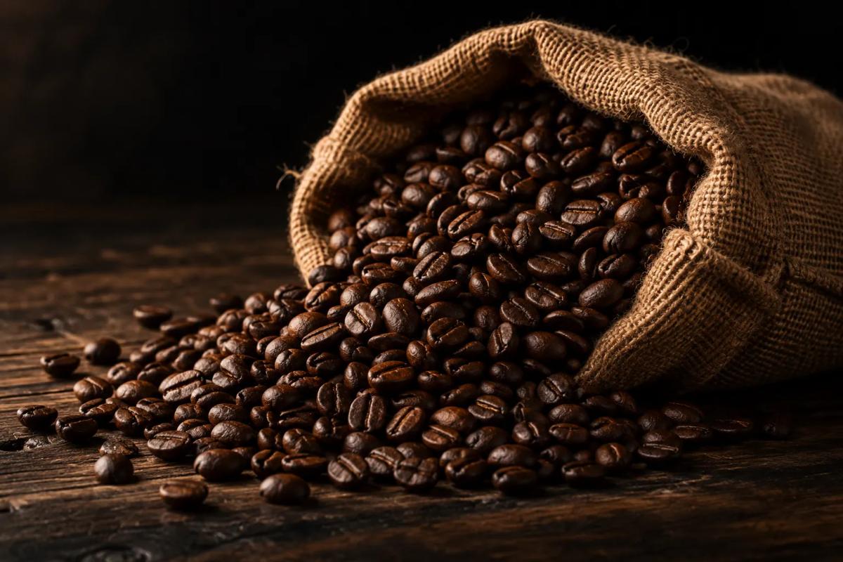 Open burlap sack full of roasted coffee beans on a dark wooden table