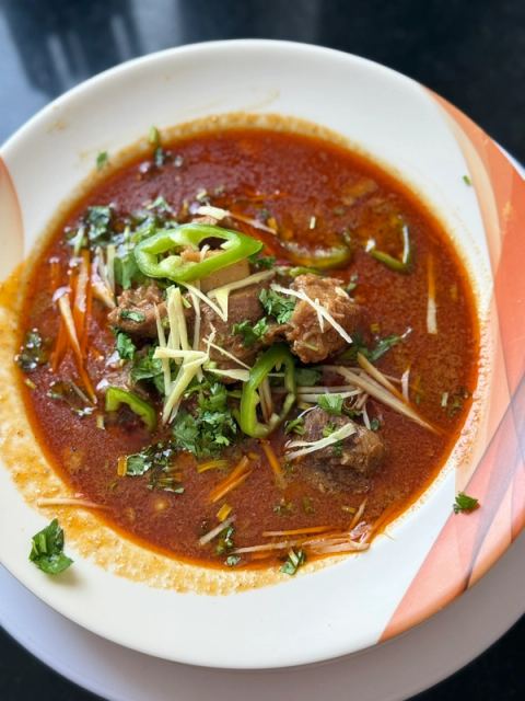 A bowl of rich mutton nihari with tender pieces of mutton in a thick, aromatic spiced gravy, garnished with fried onions and fresh herbs.