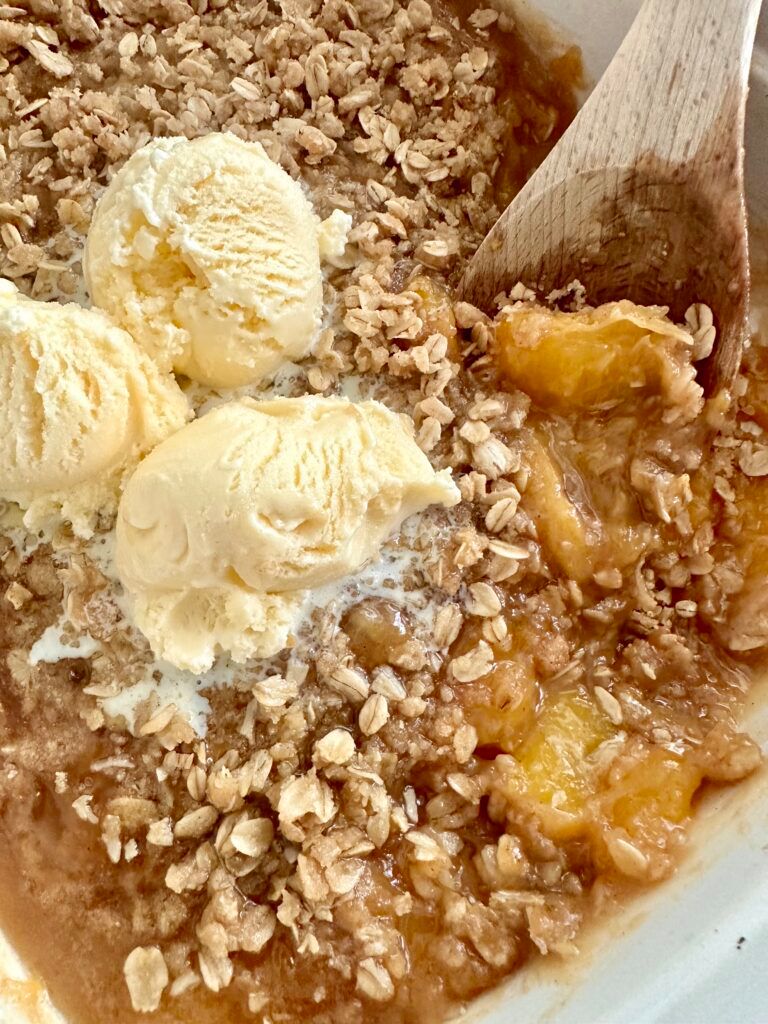 A serving of warm peach crisp with a generous scoop of vanilla ice cream