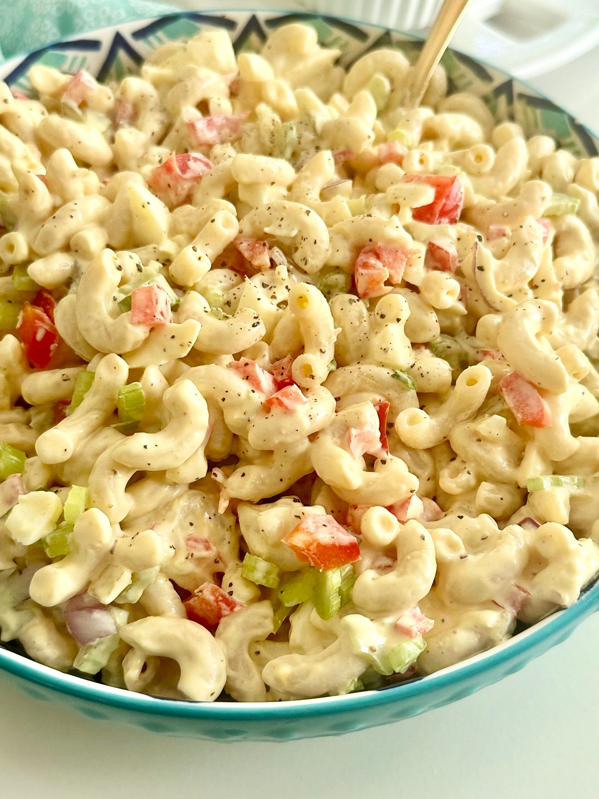 Creamy macaroni salad with chopped egg and vegetables in a patterned serving bowl