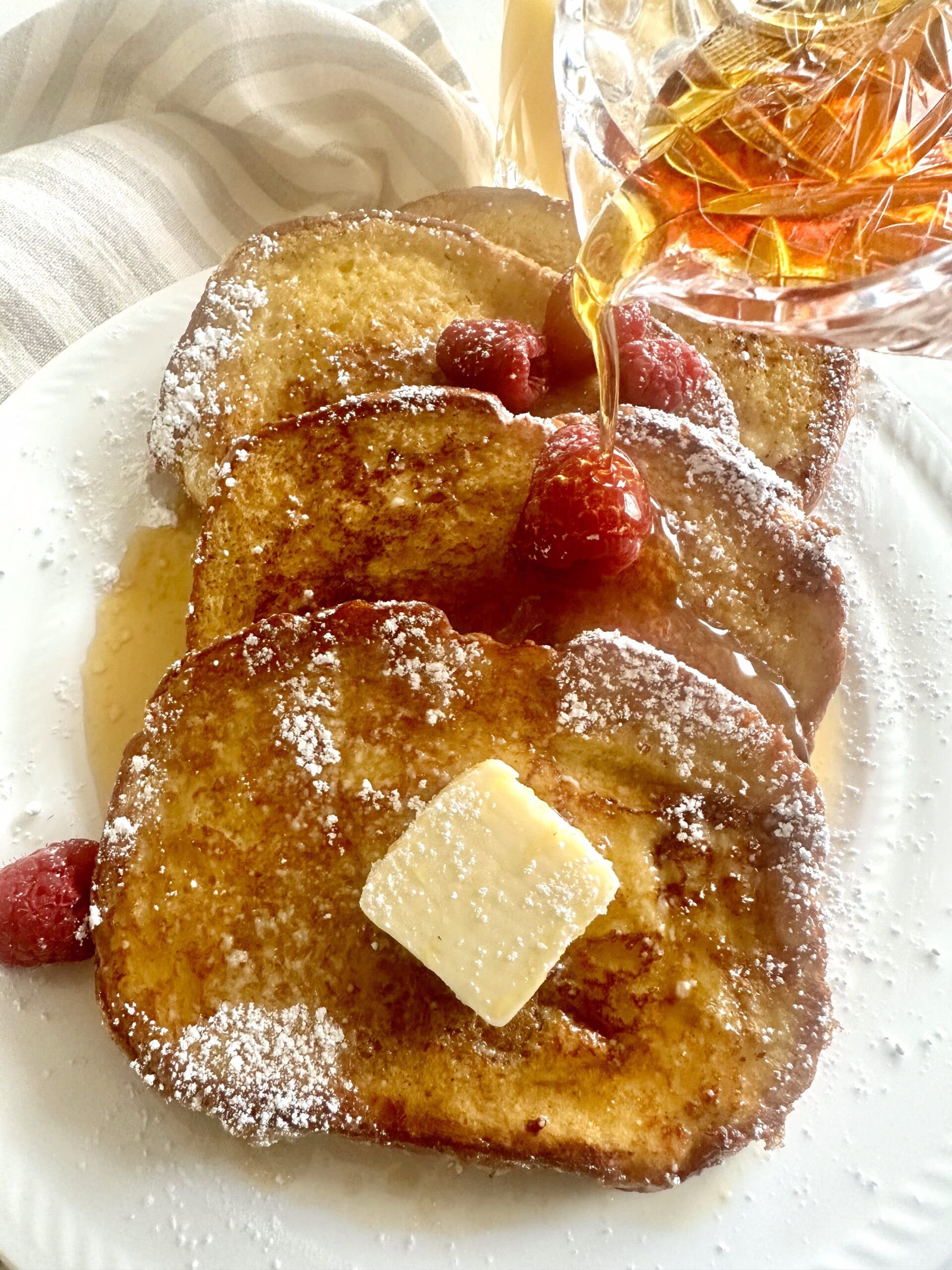 Golden brioche French toast with butter, berries, powdered sugar, and maple syrup